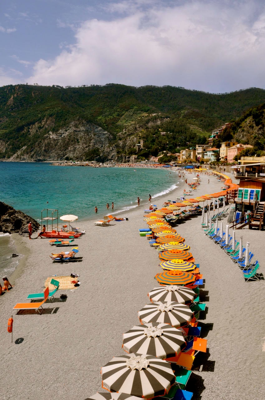 A beautiful beach with a long row of colorful umbrellas and hills in view