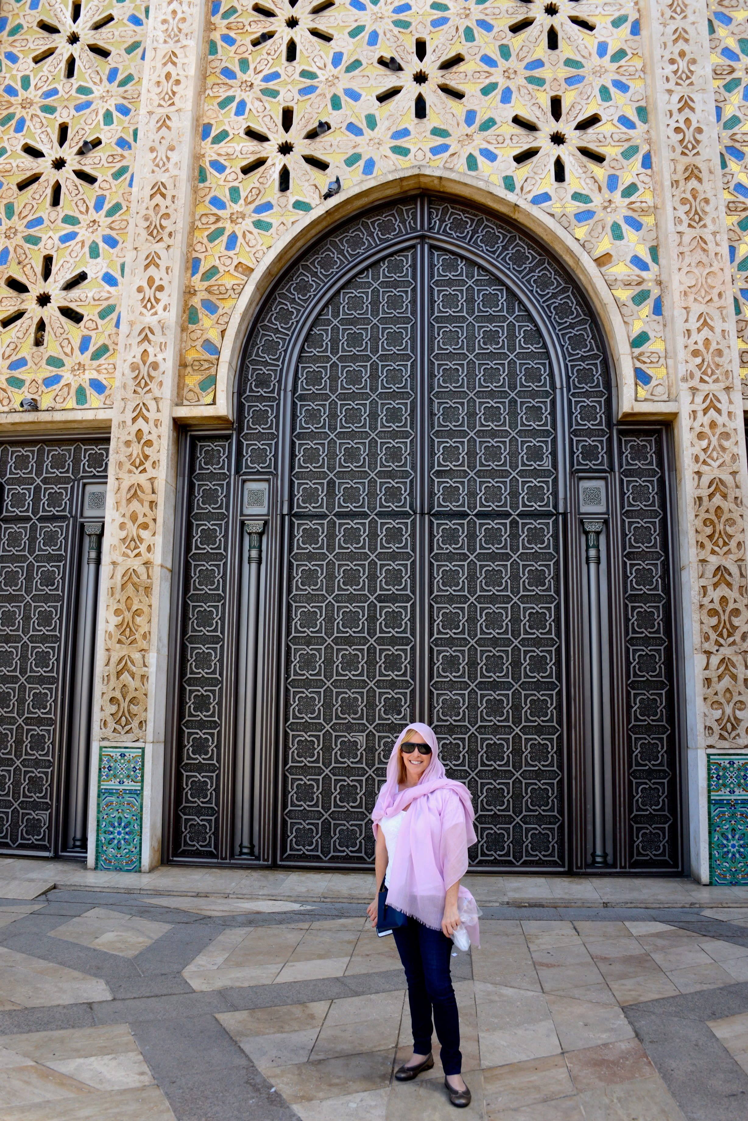 Travel advisor Allison wearing a purple shawl over her head and neck standing in front of a large arch-shaped doorway surrounded by ornate decoration