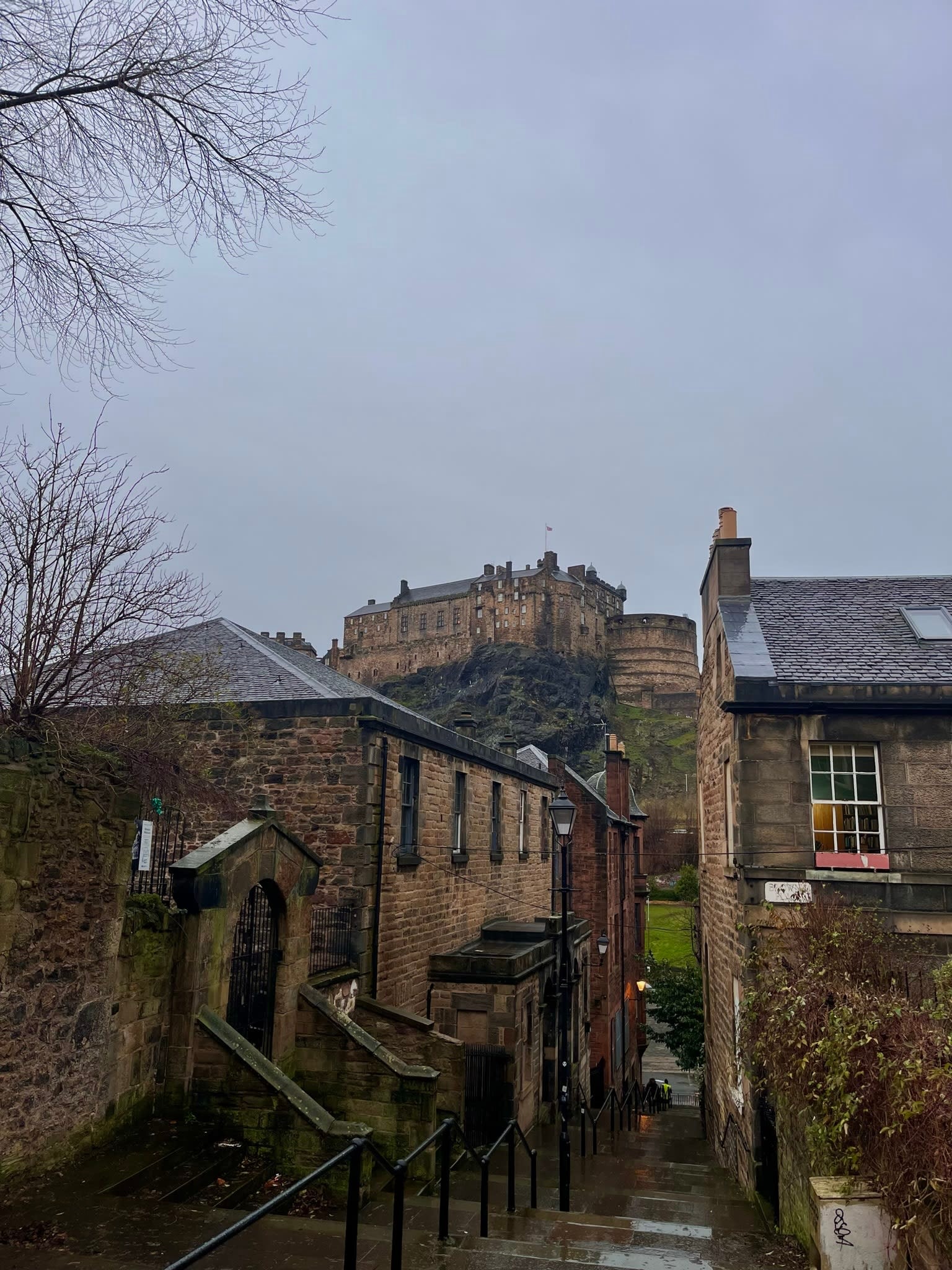 A castle on a hill on a cloudy day behind stone buildings.