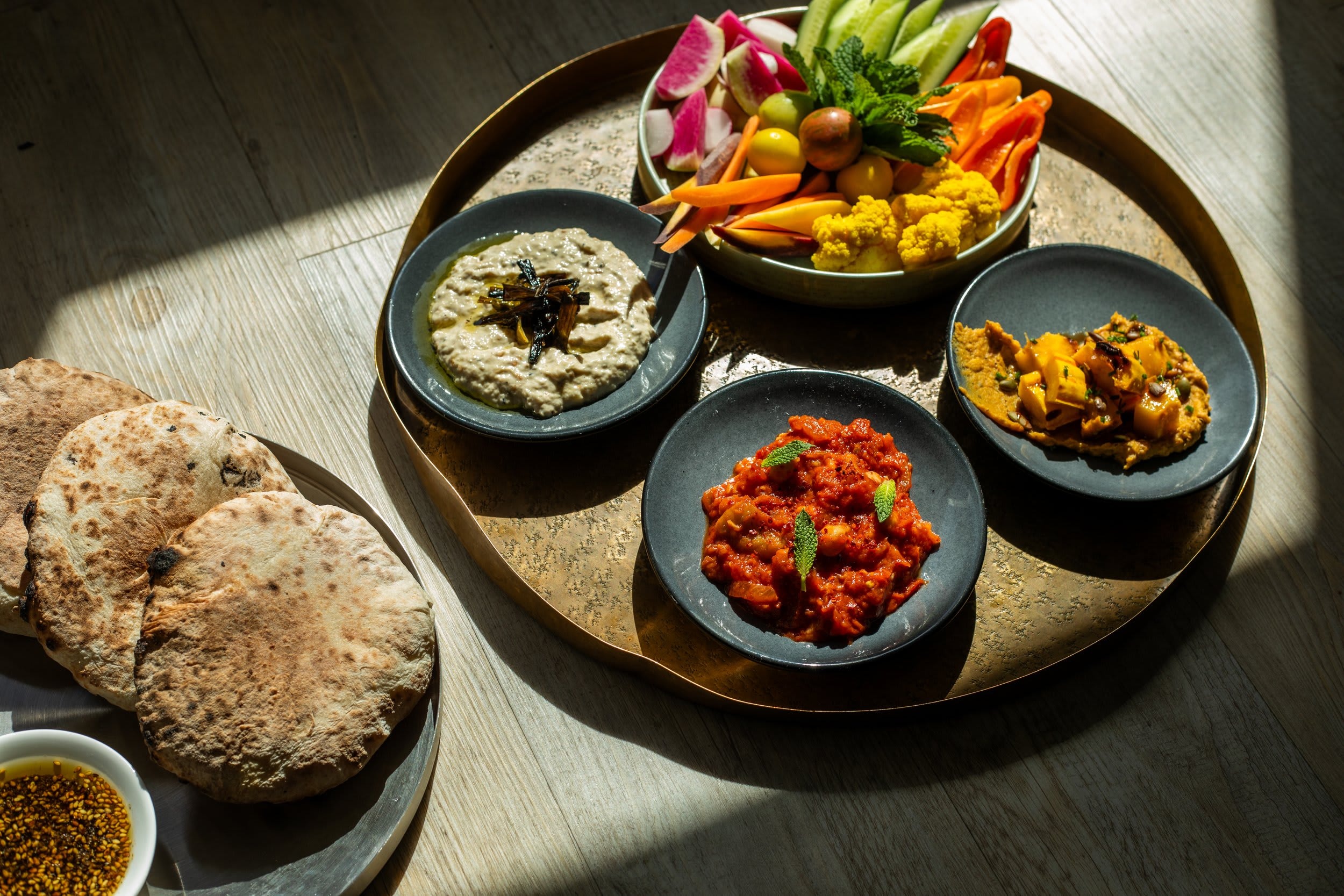 a table of food filled with pillowy pitas and colorful dips