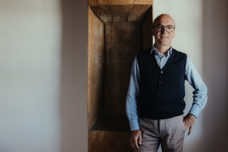 man standing in front of a white wall smiling at the camera