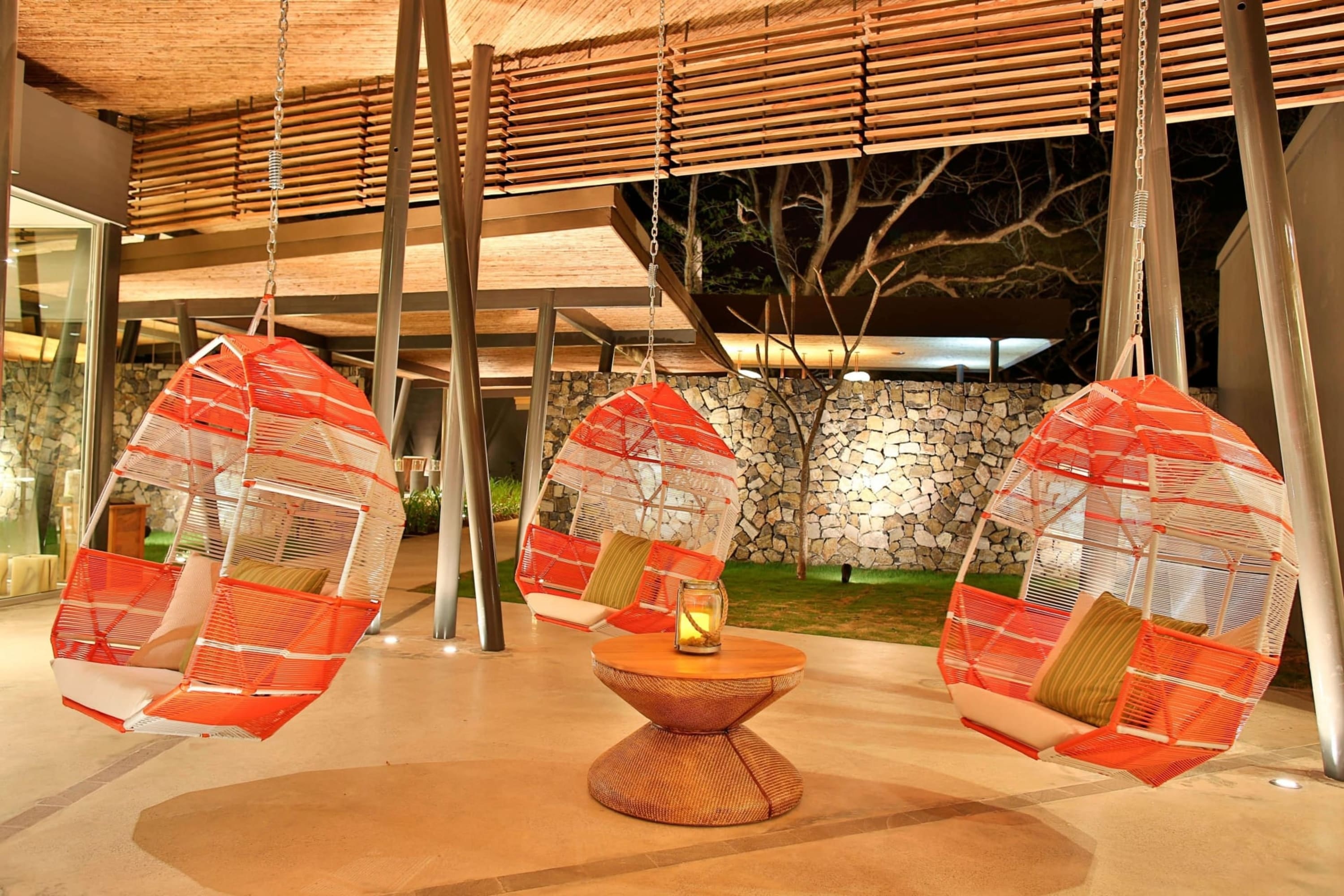 Large wicker swings hang from a well-lit, outdoor common space. If not for a small break in the awning, you'd assume it was daytime