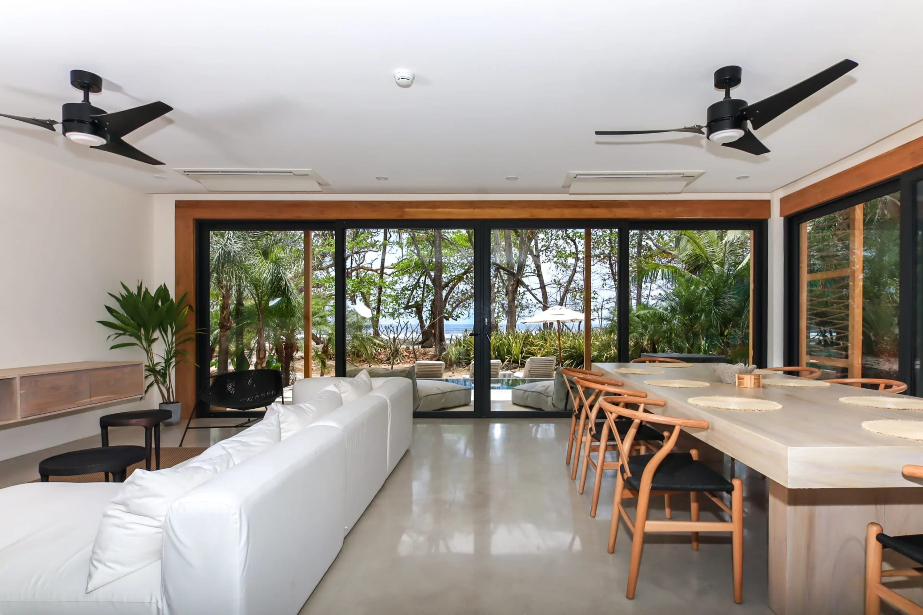 A mix of chic contemporary and jungle-inspired furnishings within a vast living and dining area. The room, separated by glass doors, opens up to an outdoor  space with a private pool