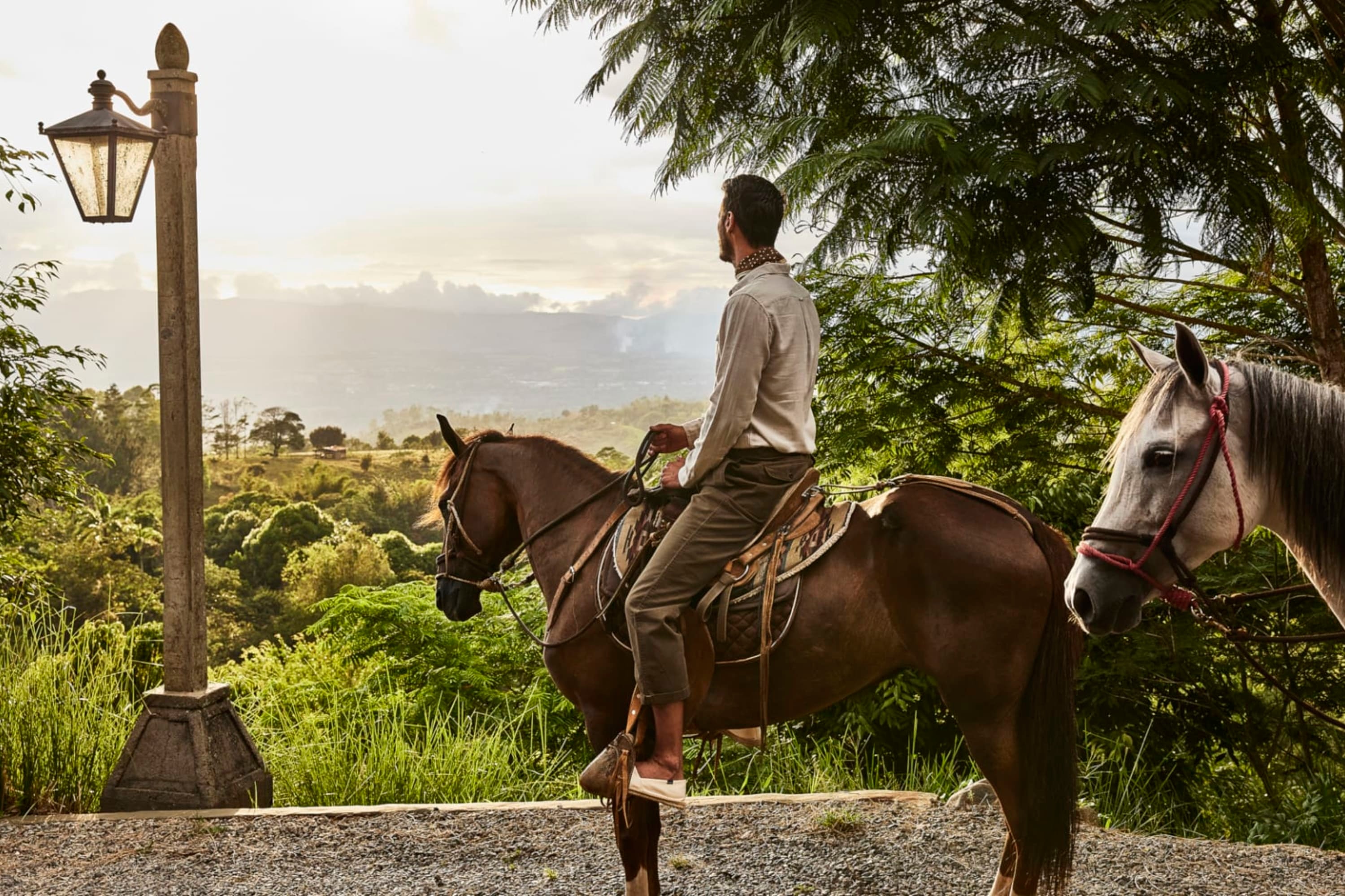 A man on horseback looks out over vast swathes of lush Costa Rican jungle from a vantage point at Hacienda AltaGracia, Auberge Resorts Collection