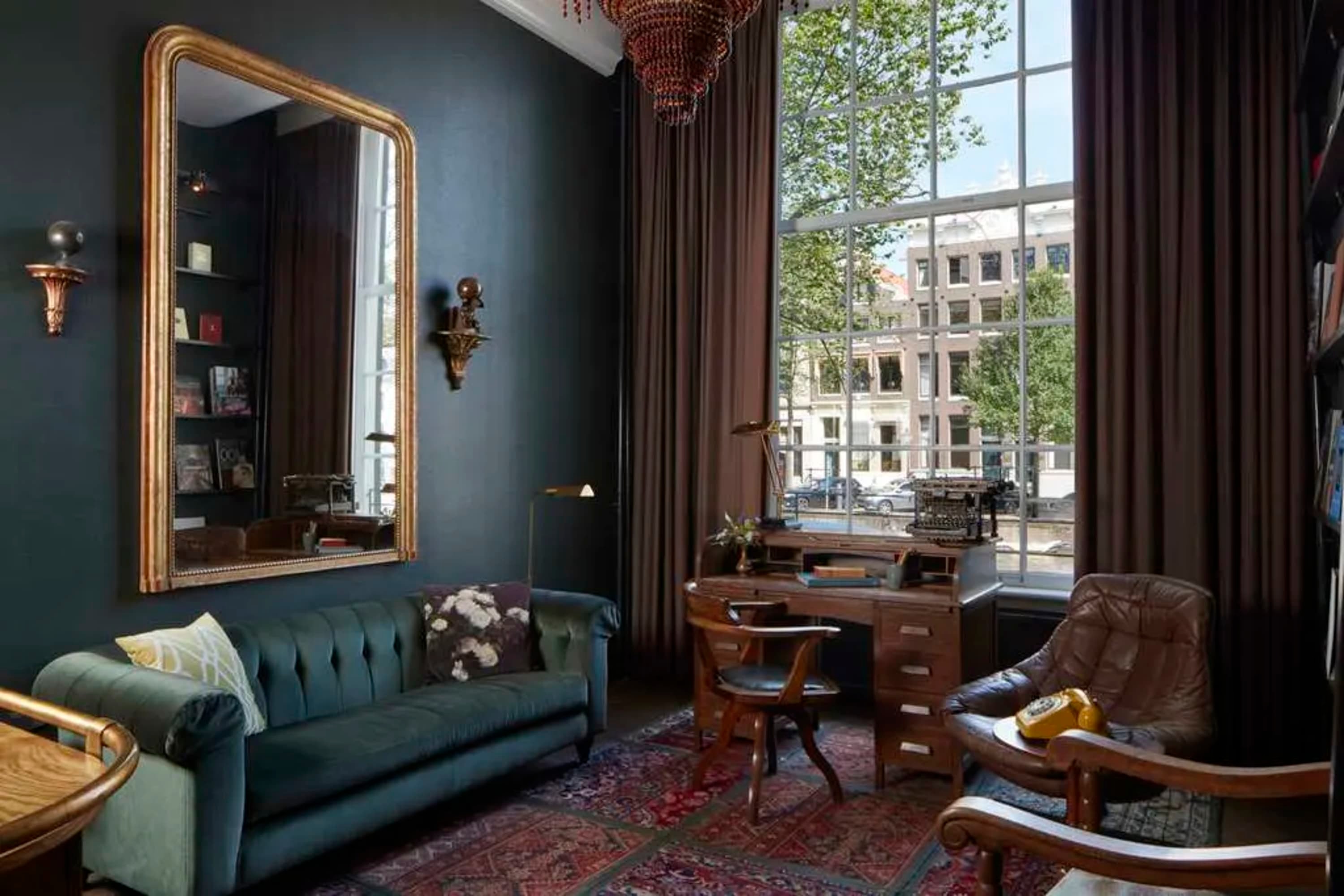 Moody lighting, vintage furniture and Gilded Age decor in a cozy but elegant common space with views of Amsterdam's historic architecture