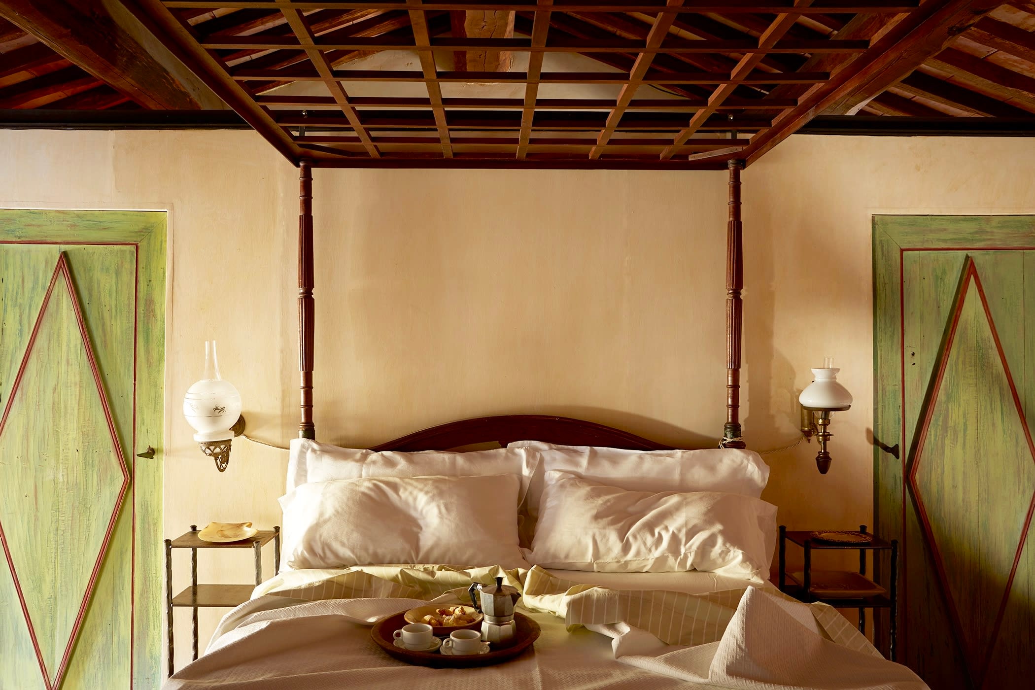 a tray of coffee and breakfast rests on a luxe four-poster bed