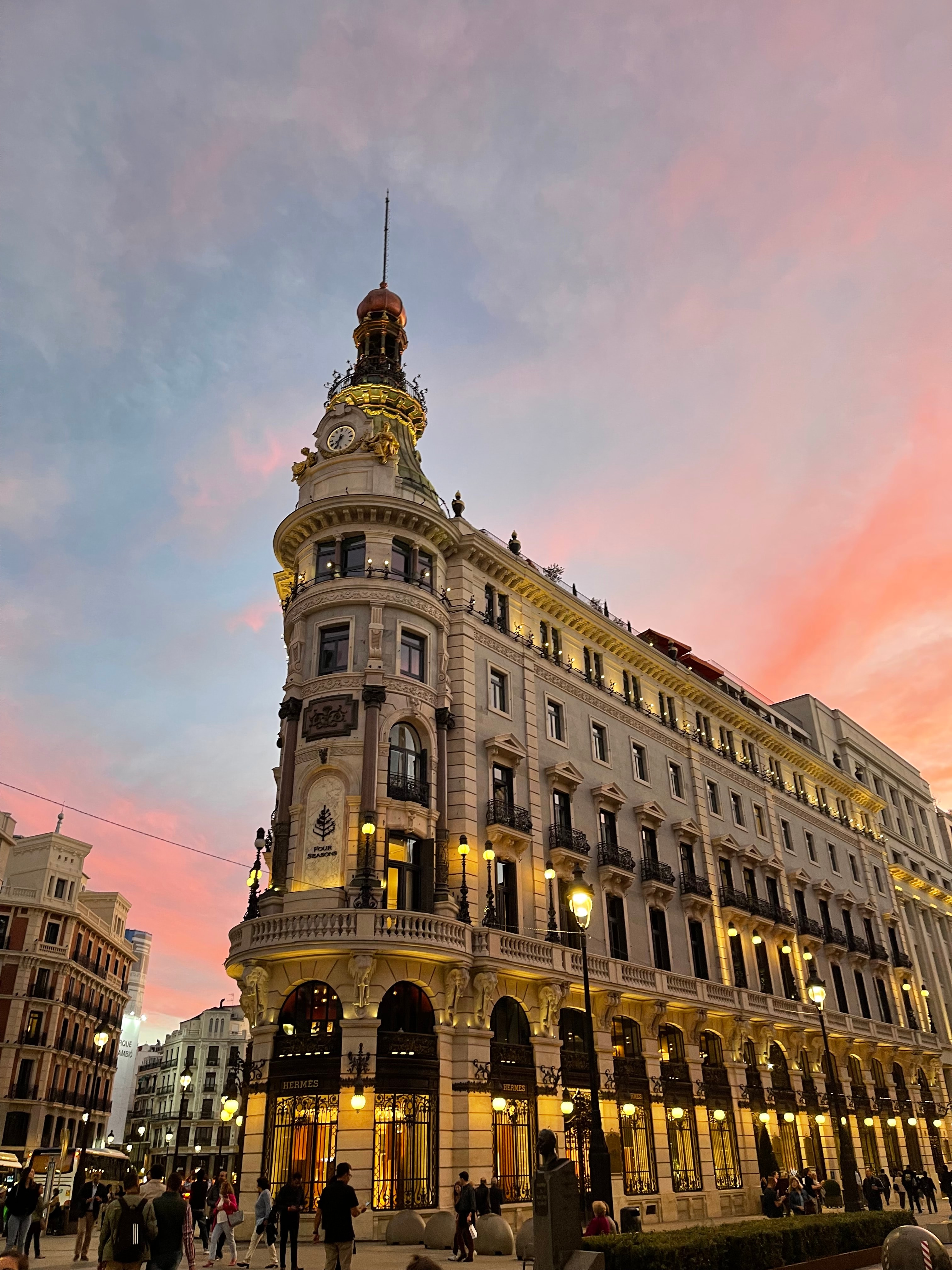 A view of a building exterior lit up at dusk with a pink sunset in the background. 