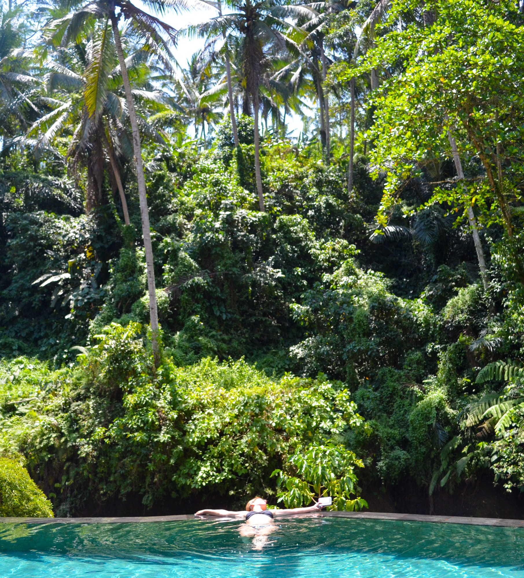 Travel advisor Sofia lying in a swimming pool surrounded by lush foliage