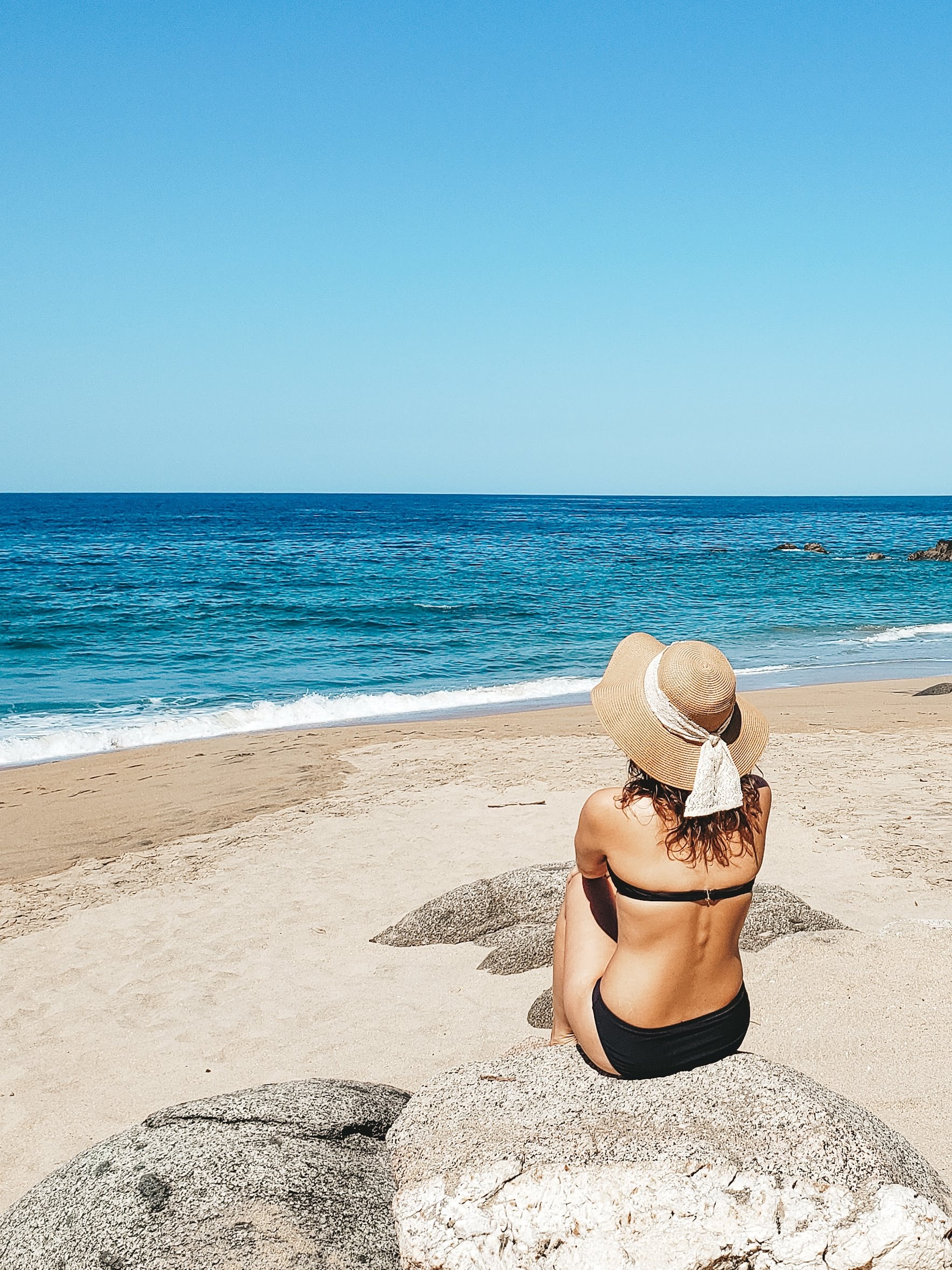 Advisor sitting on the beach in a black swimsuit and a sun hat with the ocean in the distance.