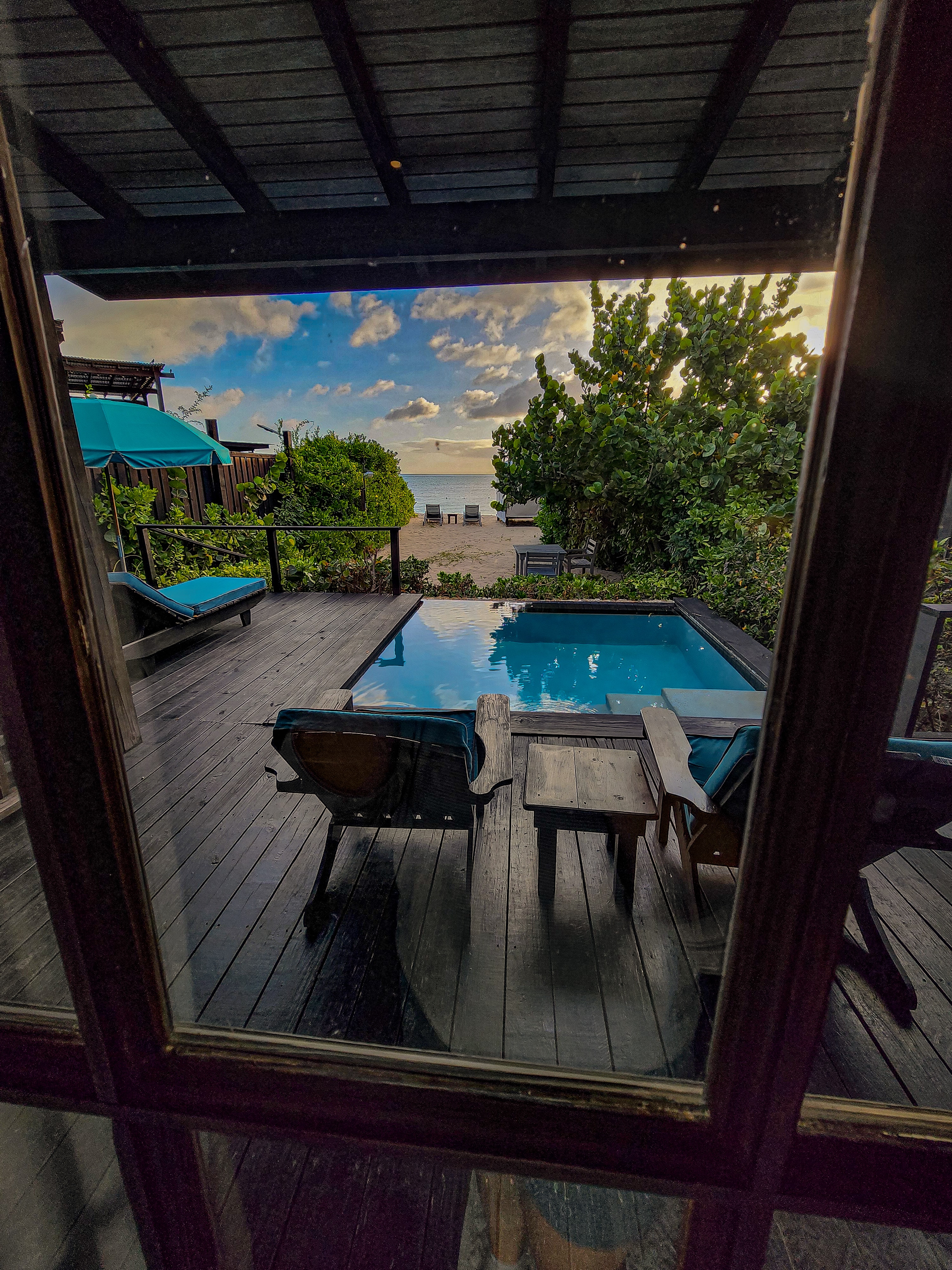 An image of a pool at sunset with loungers and foliage in the distance. 