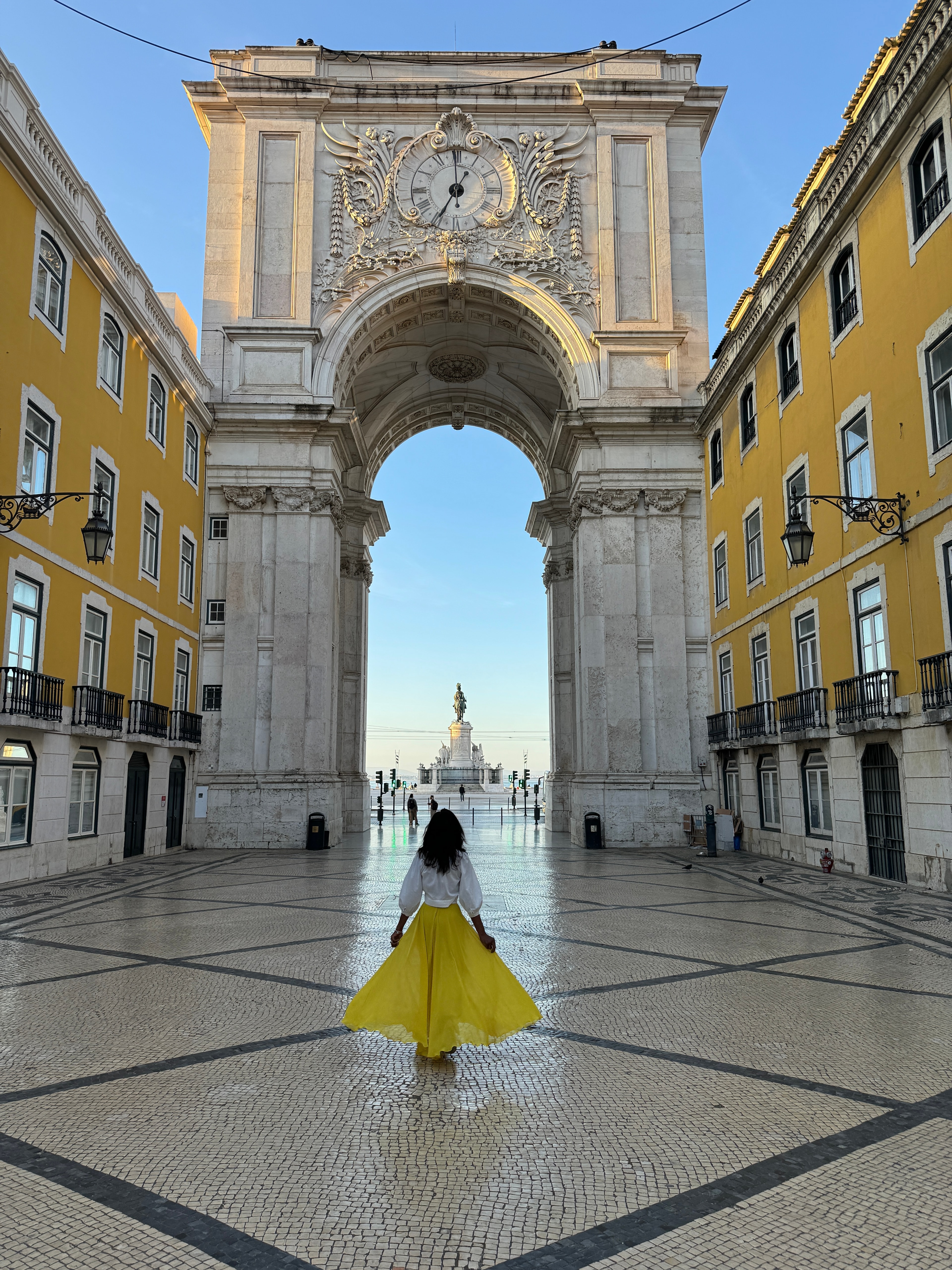 Advisor in a bright yellow skirt walking through a large open square with yellow buildings and a classic archway. 