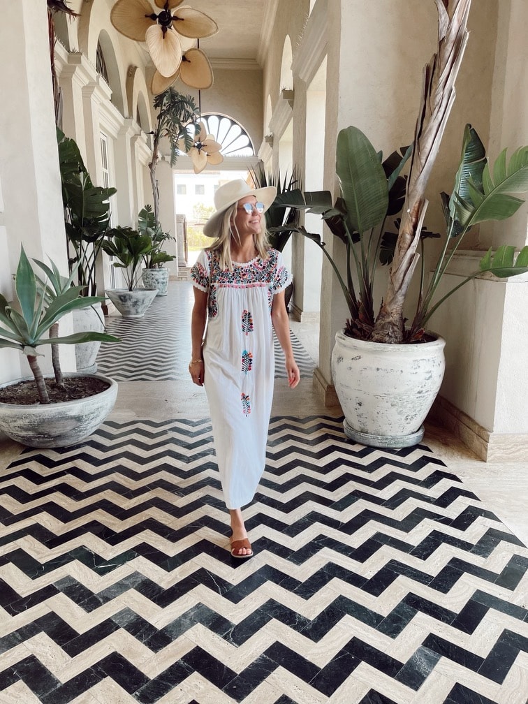 Travel advisor Sara walking on a black and white tiled floor in a beautiful white hallway with large plants and hanging light fixtures