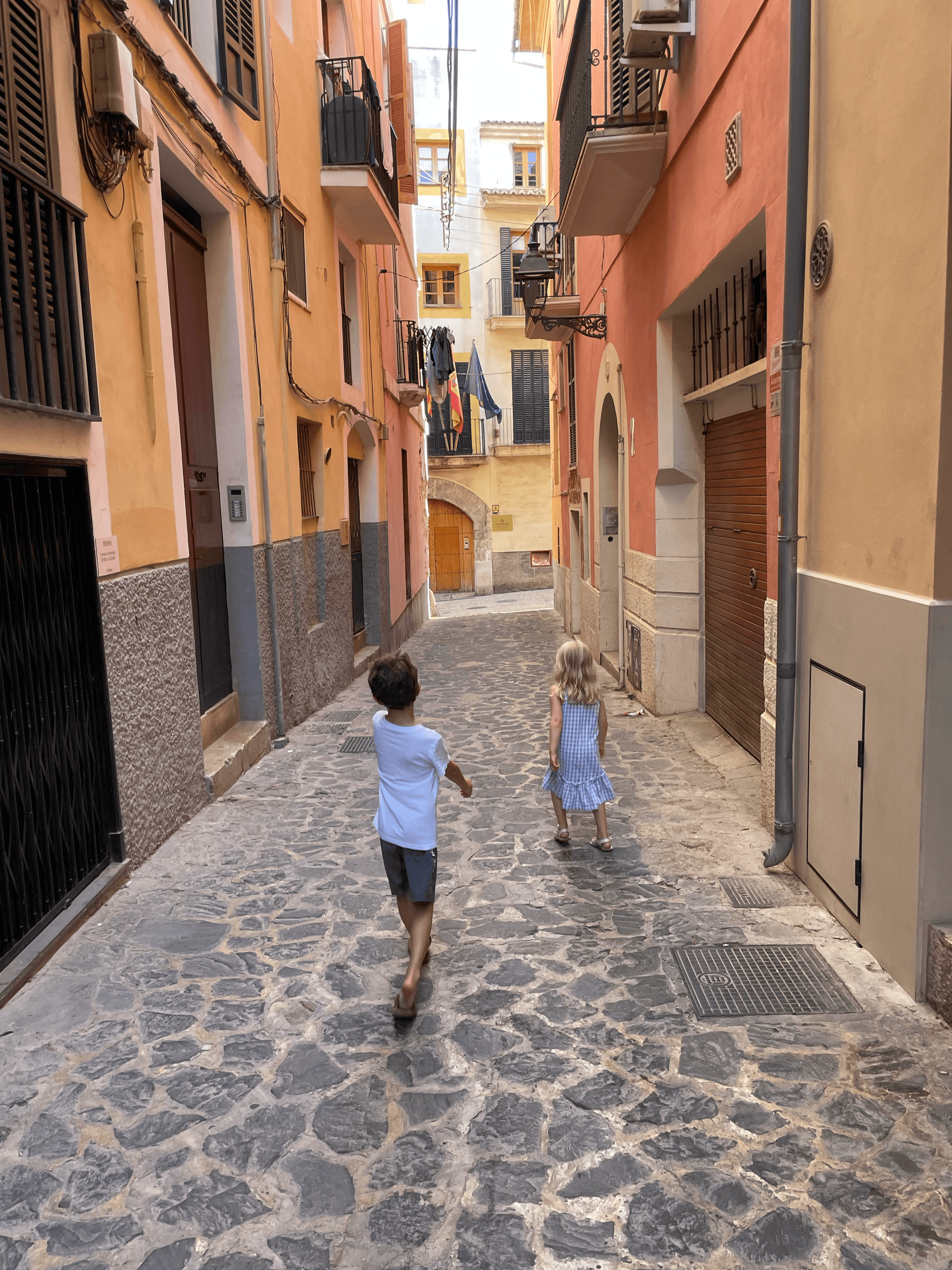 Two children walking down a quaint, narrow street in between red and orange colored buildings