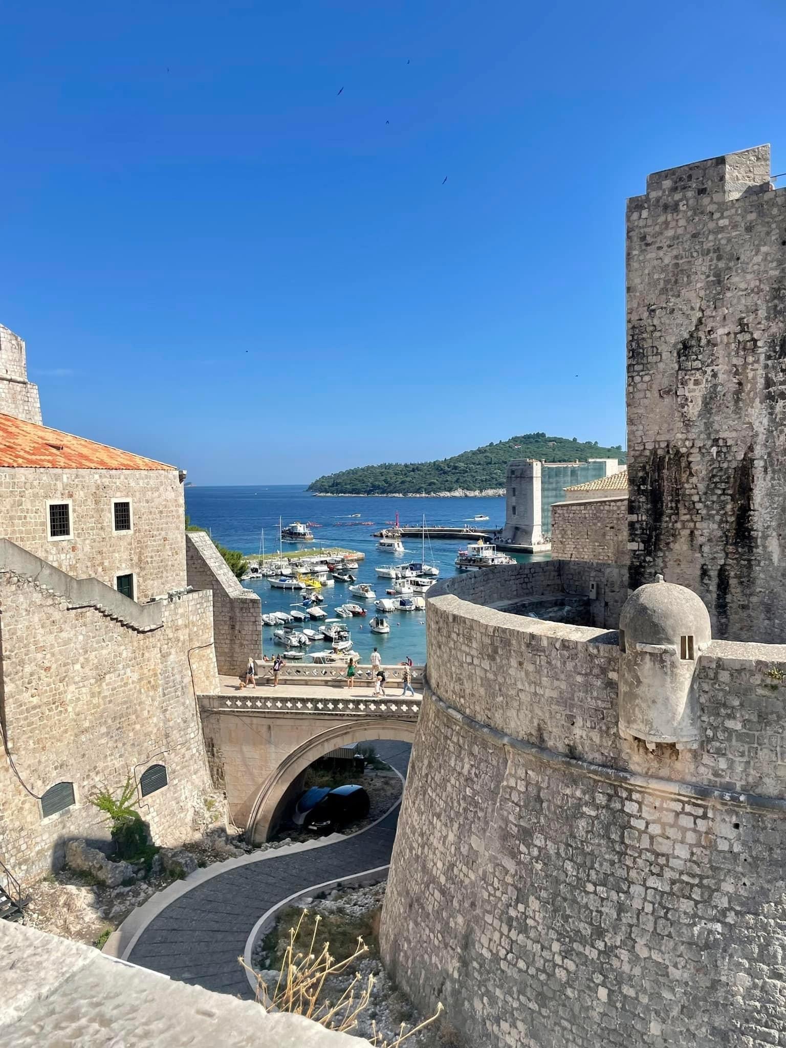 View of a winding street through old stone walls leading down to the sea on a sunny day