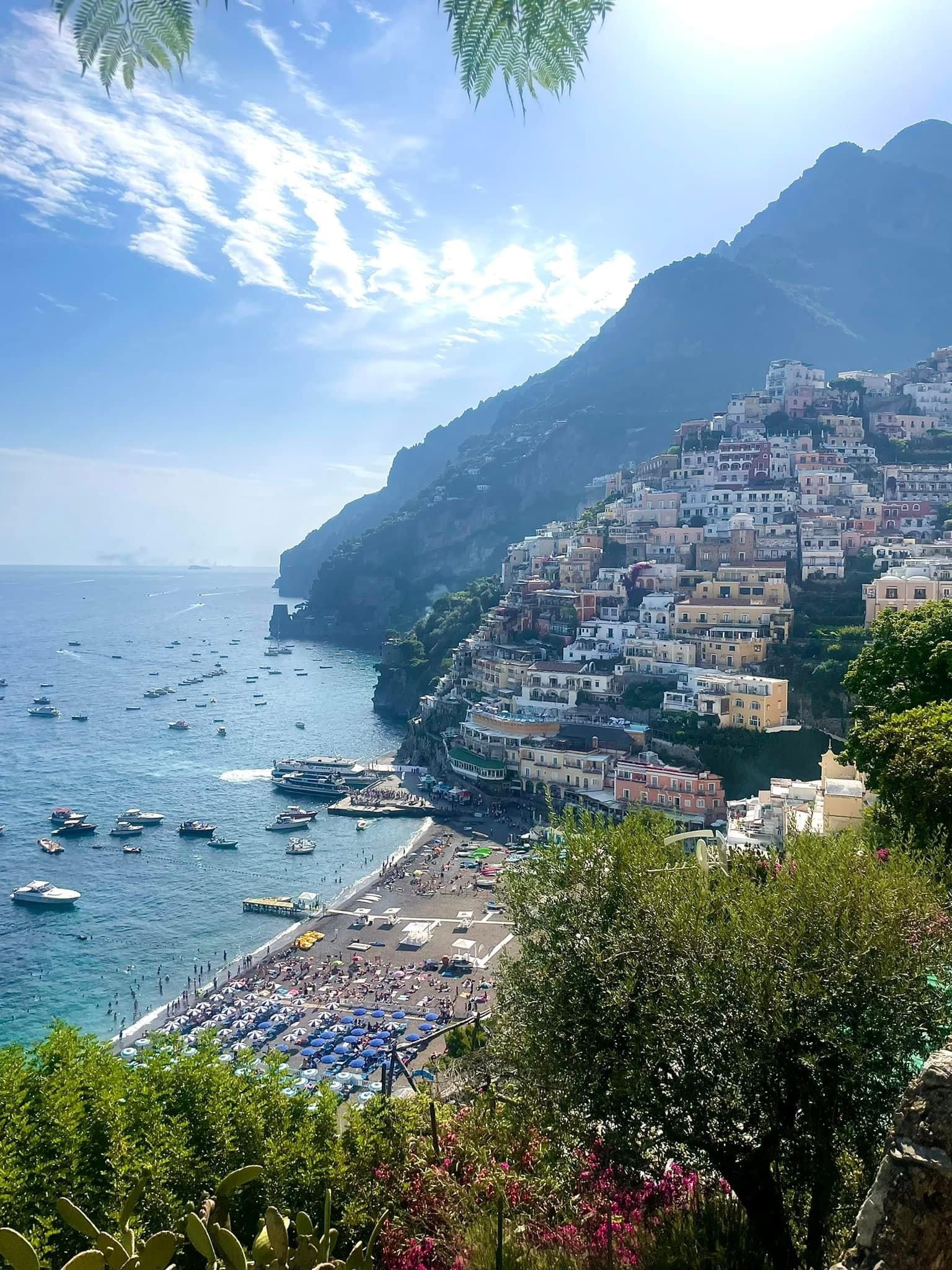 Pretty view of colorful coastal houses on a mountain rising above the sea and beach with several boats seen floating offshore