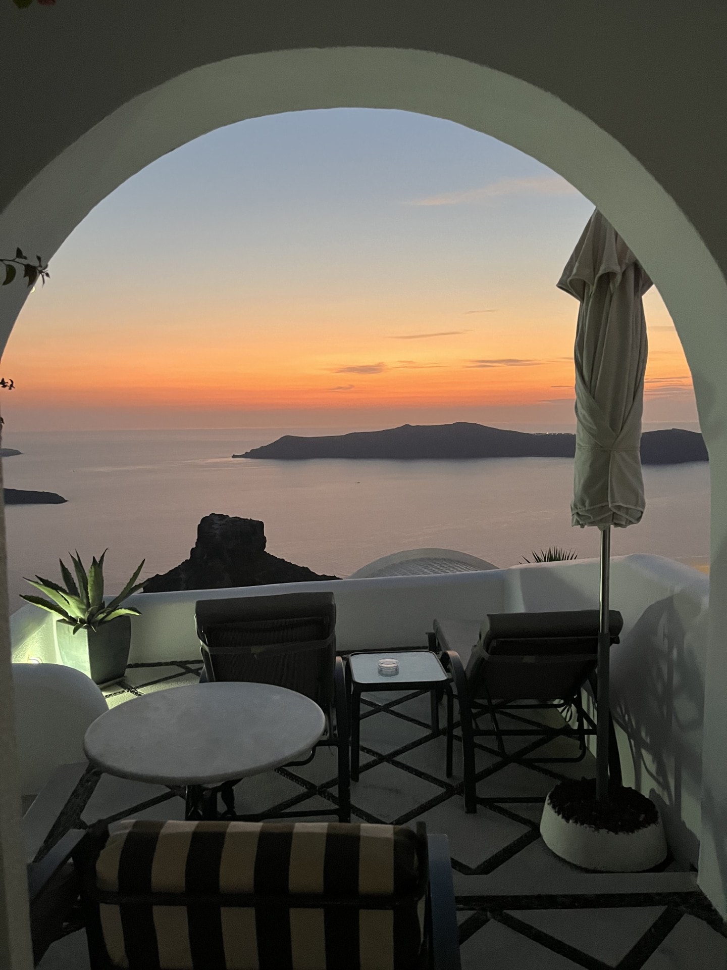 A Greek balcony with patio furniture overlooking the ocean at sunset.