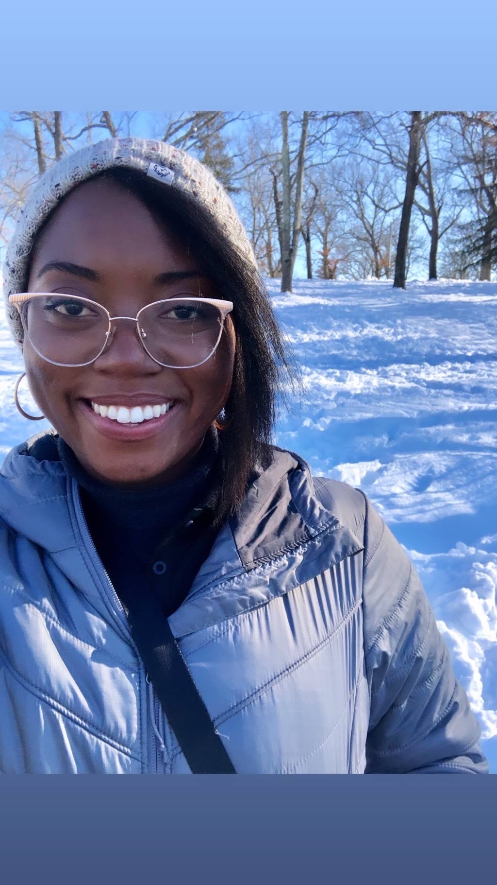 Selfie of Ashlyn in a snow jacket and beanie in a snowy field.