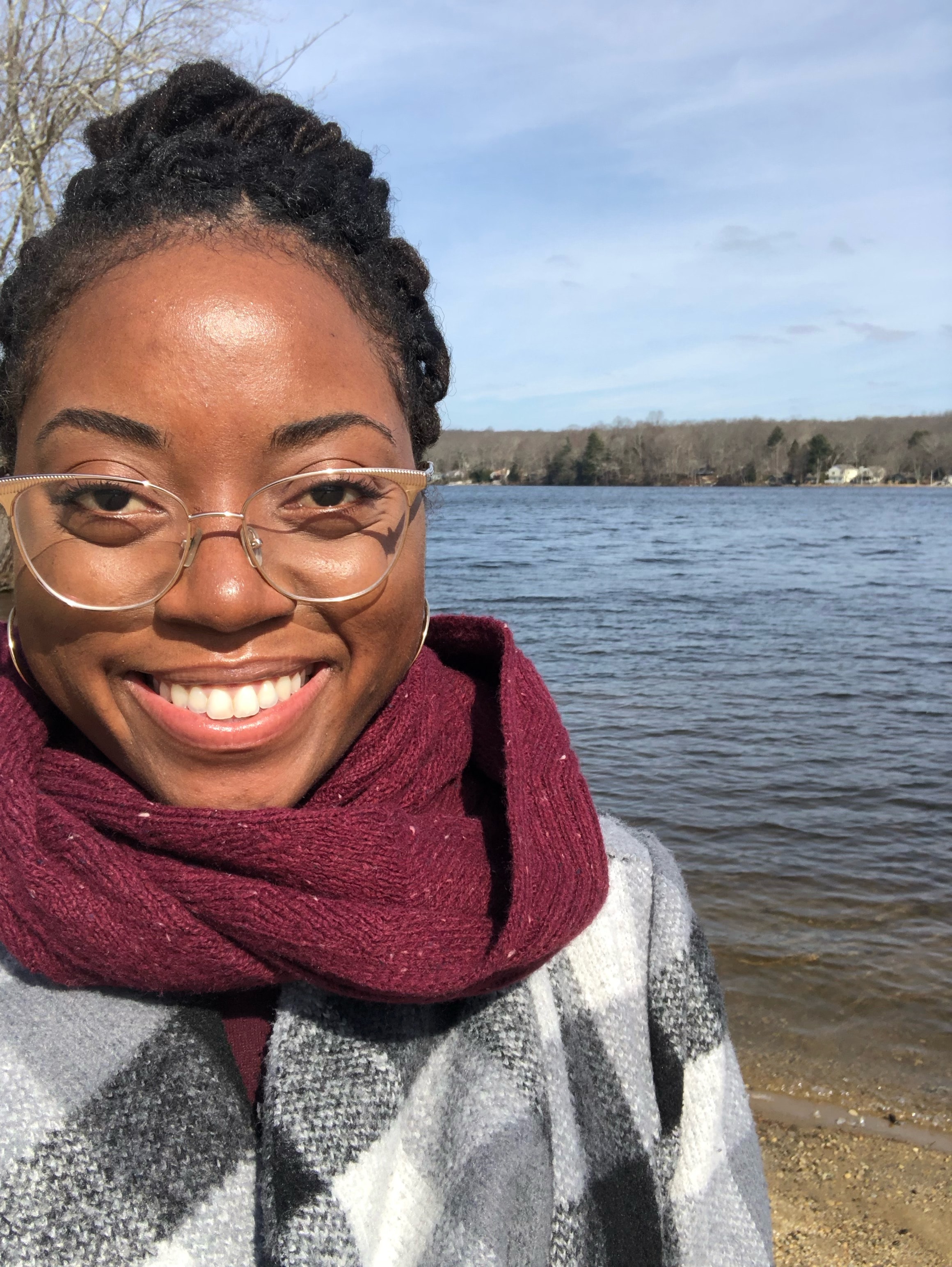 Selfie of Ashlyn in a black and white jacket and red scarf standing next to a lake.