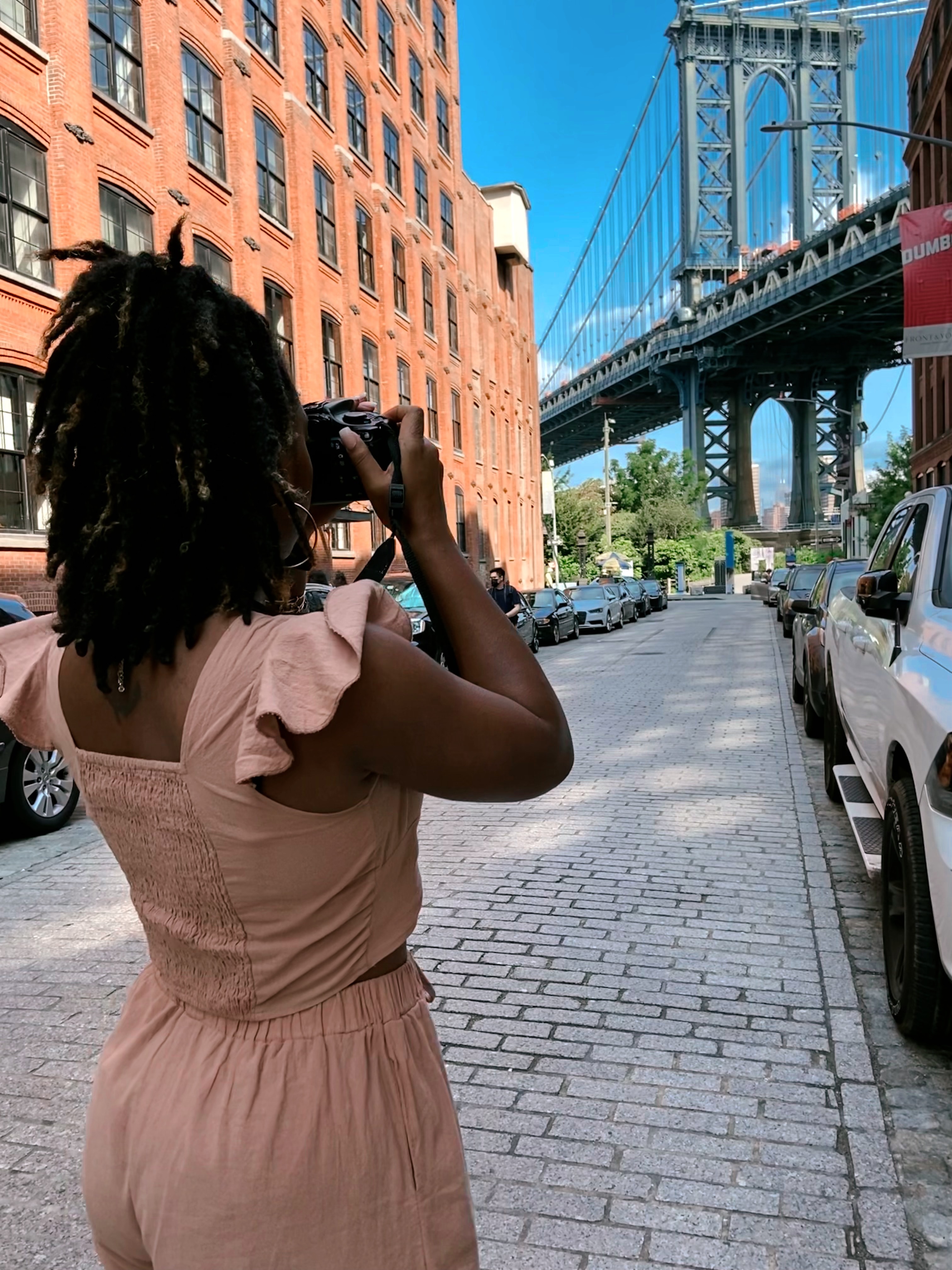 Ashlyn holding a camera taking a photo of the Brooklyn Bridge.