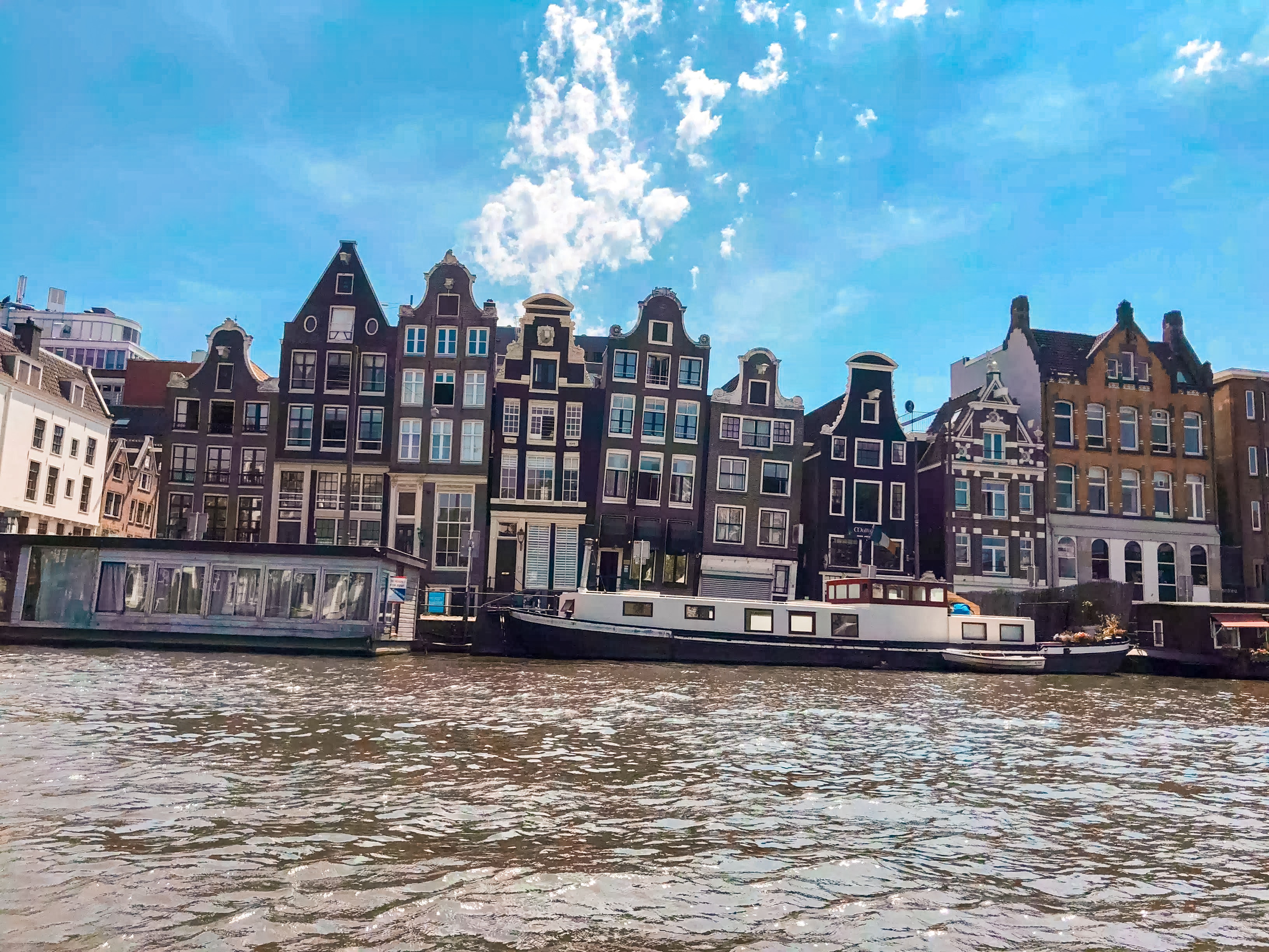 An image of tall, narrow buildings across a waterway with boats docked.