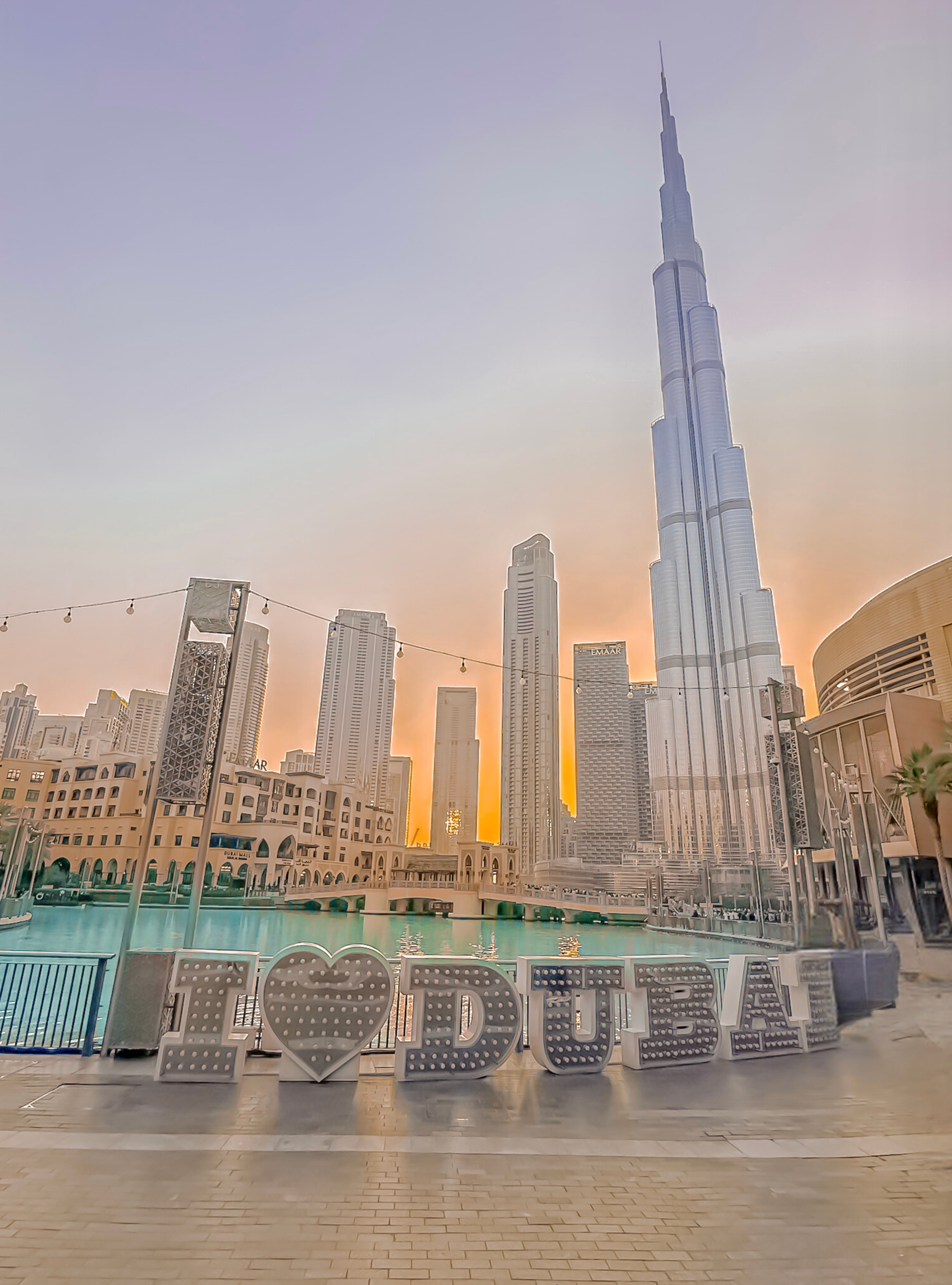 A view of tall buildings in Dubai at sunset with a pool in the distance. 