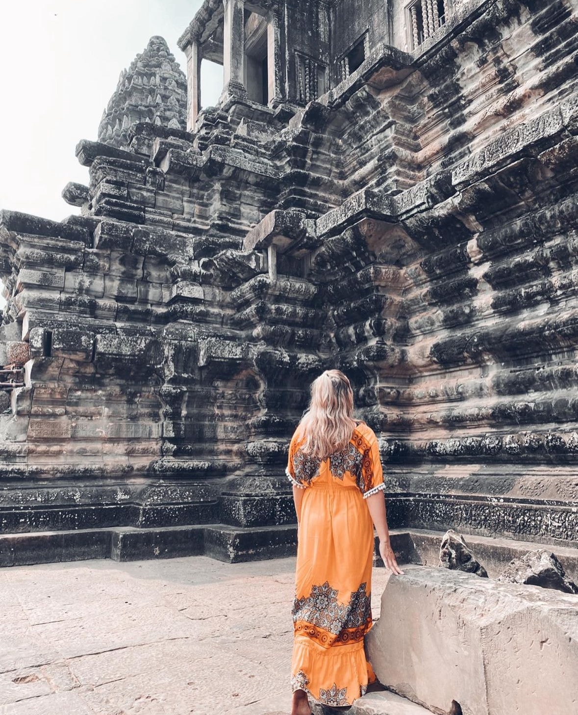 Advisor posing for an image in front of ancient ruins in an orange dress during the day time. 