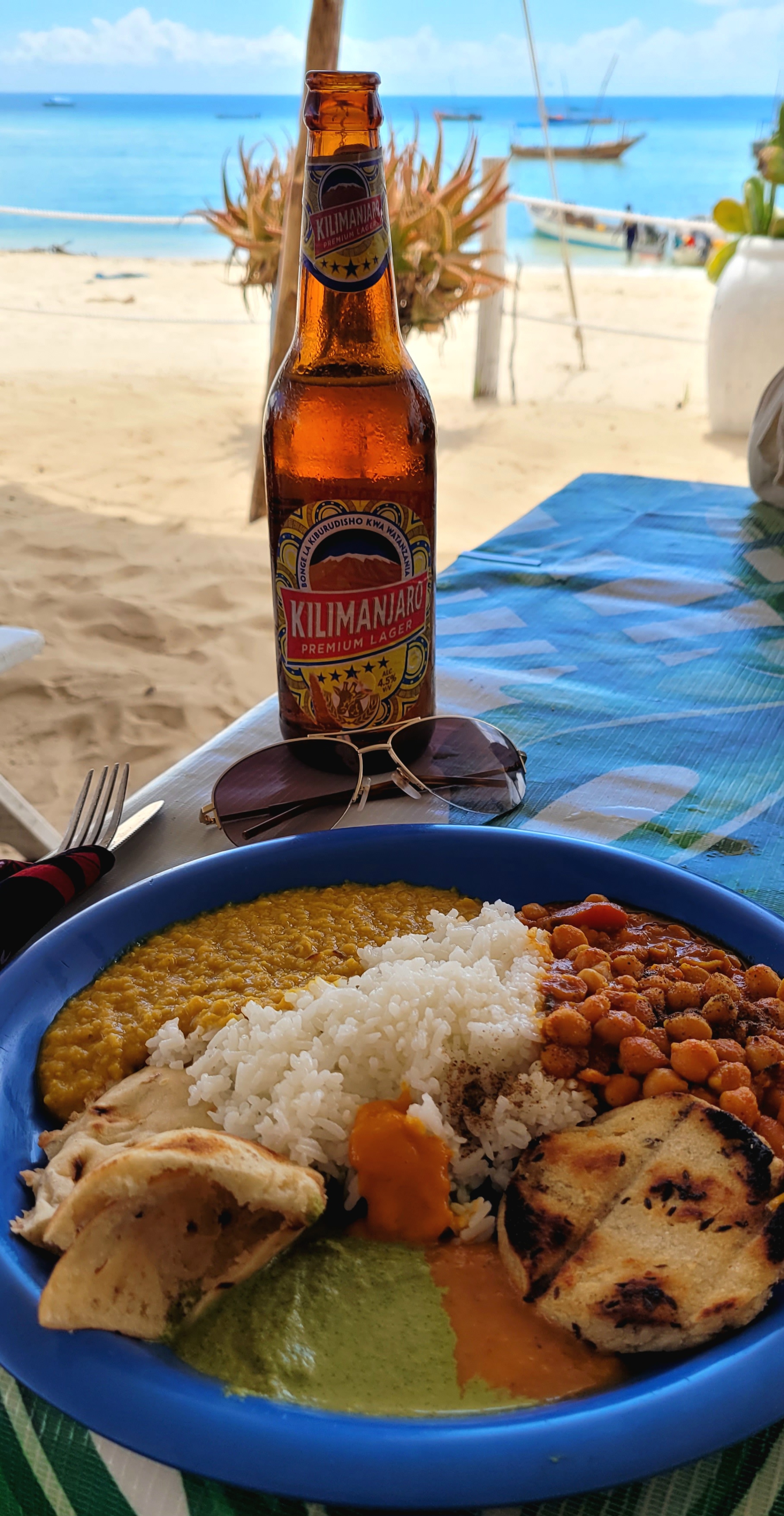 An image of delicious food with a cold beer on a table near the beach on a sunny day.