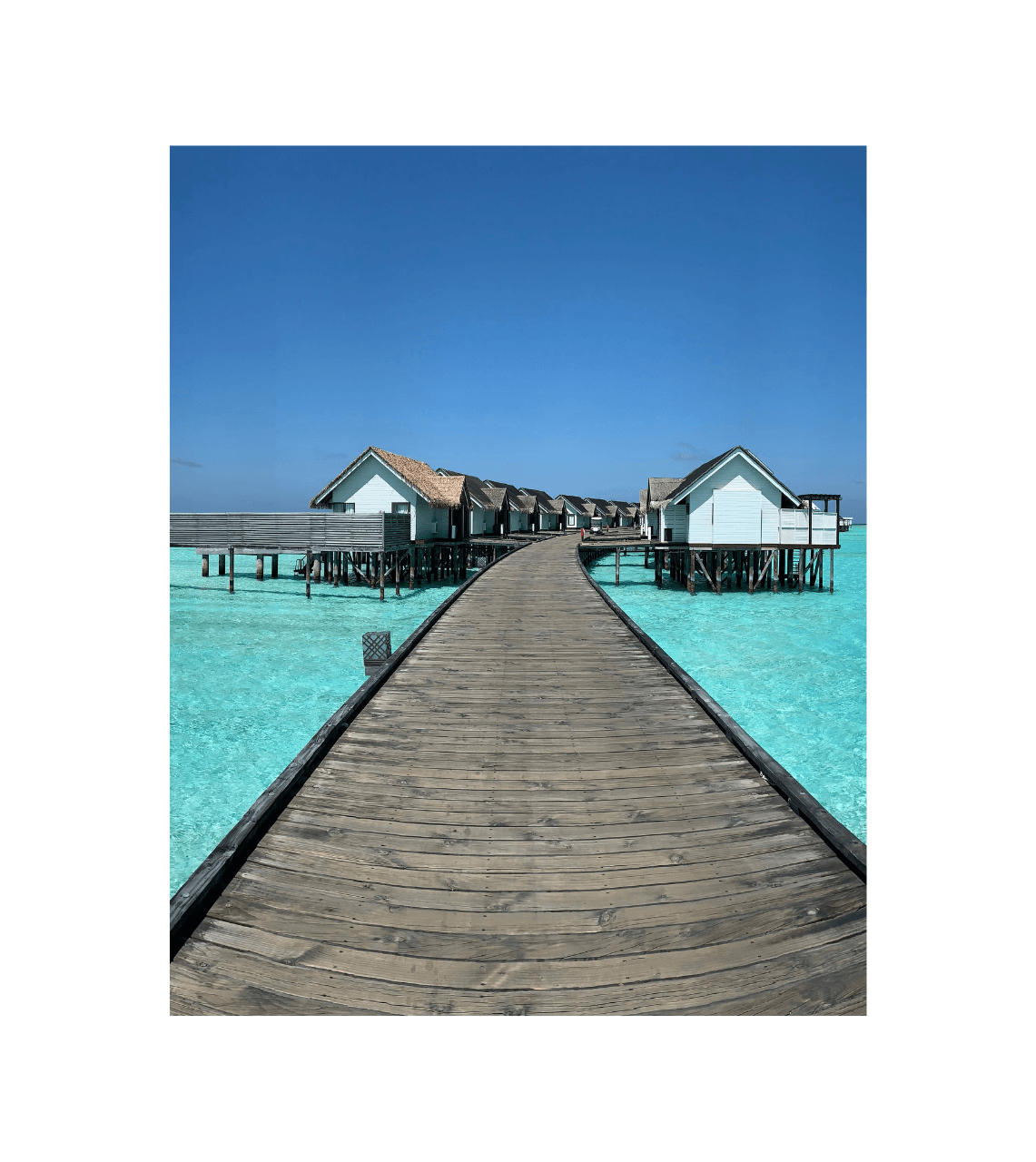 An image of a walk way on a sunny day with the clear ocean with resort rooms above the ocean.