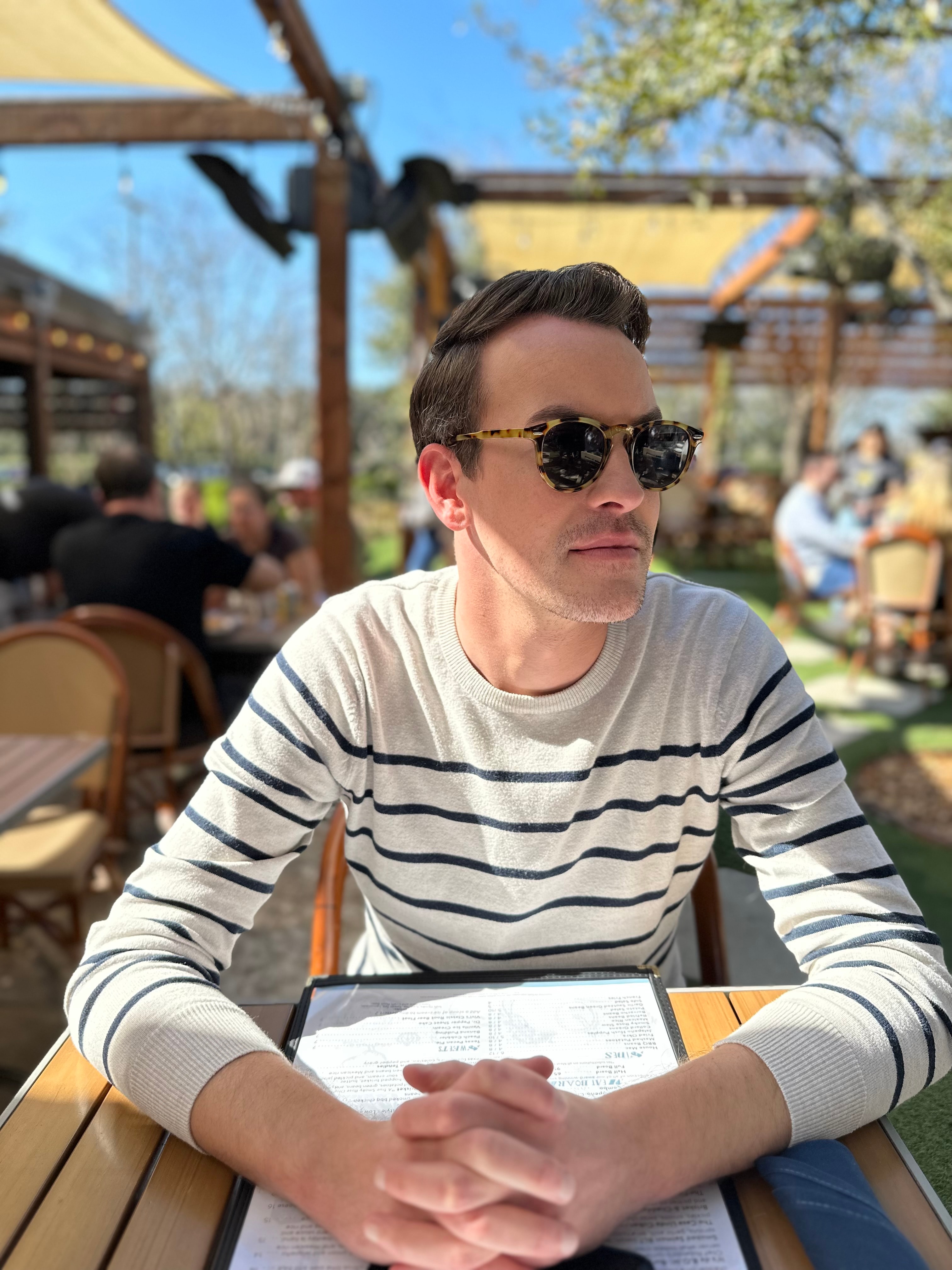 Advisor posing for an image in a striped shirt sitting at an outdoor restaurant on a sunny day. 