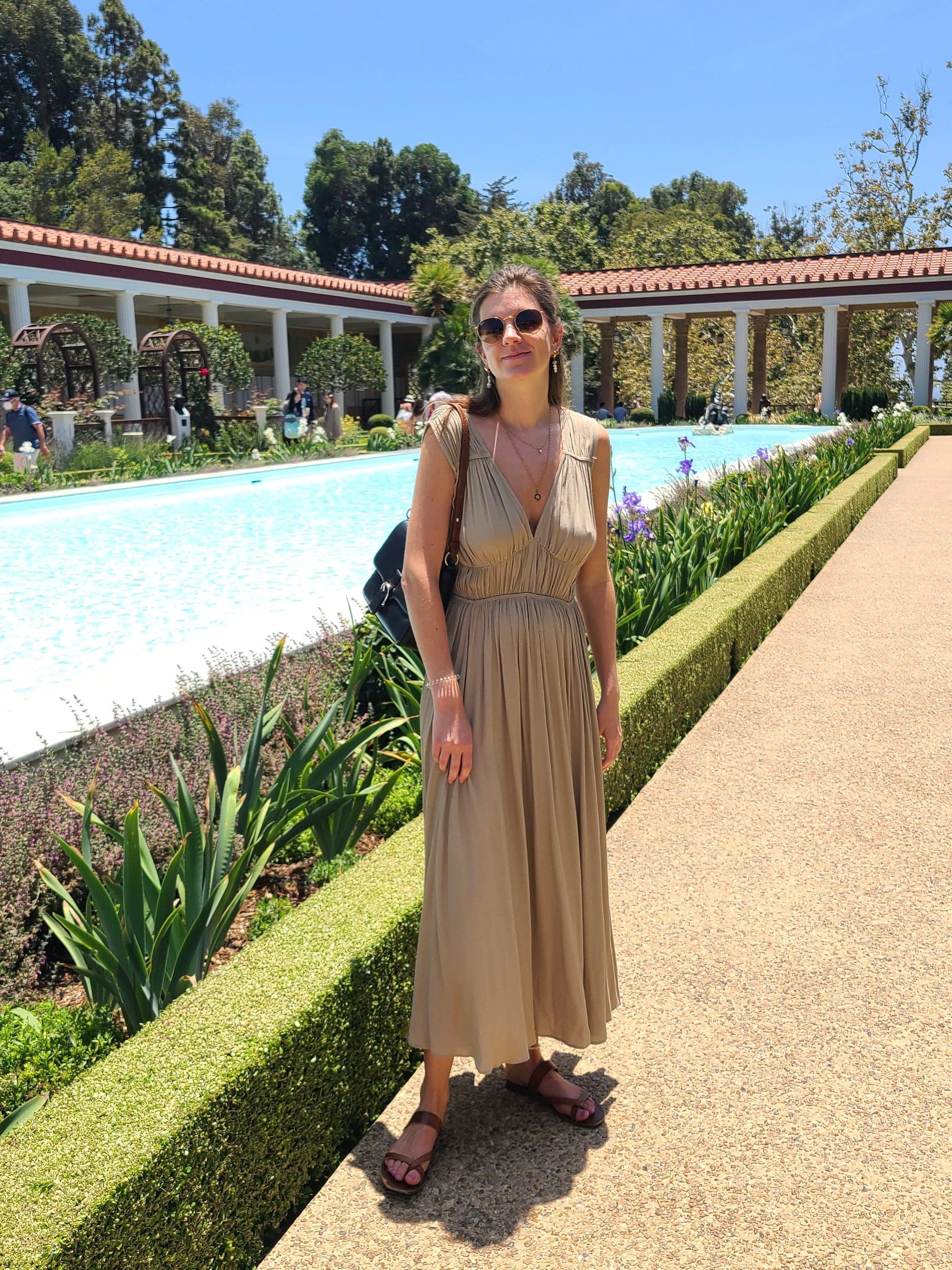 Advisor posing for an image in a brown dress with a pond and a building with arches in the distance during the daytime.