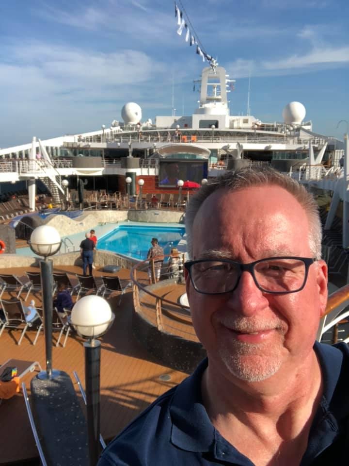 Advisor posing of a photo on a cruise ship on a sunny day with a pool in the background. 