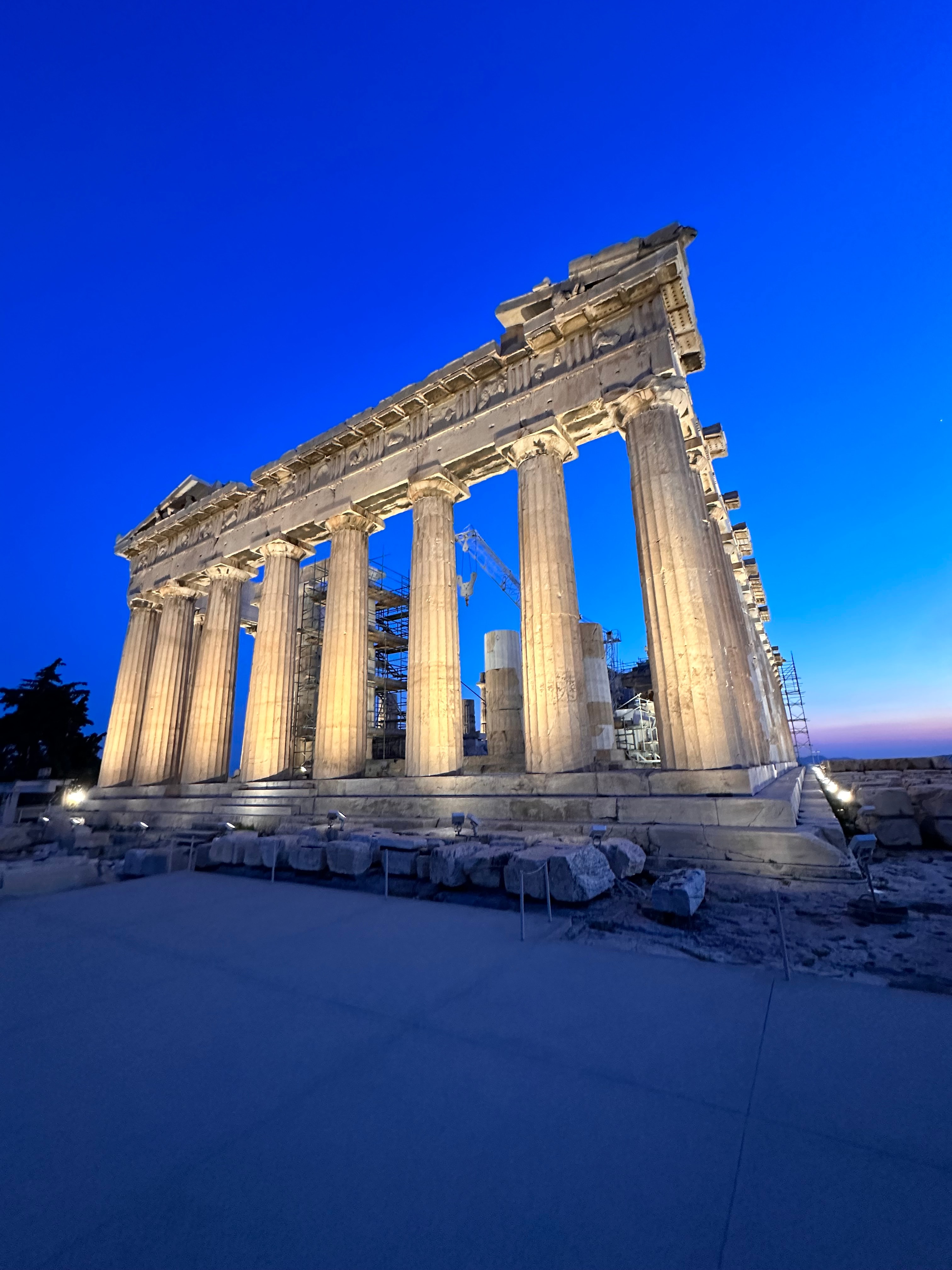 View of ancient columns lit up at night against a deep blue sky