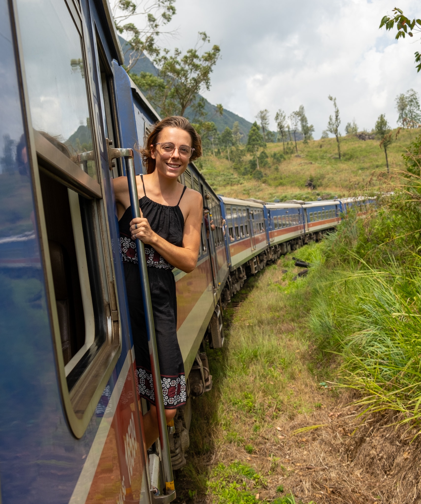 Advisor posing for an image outside the side of a train car moving through the country side on a sunny day. 