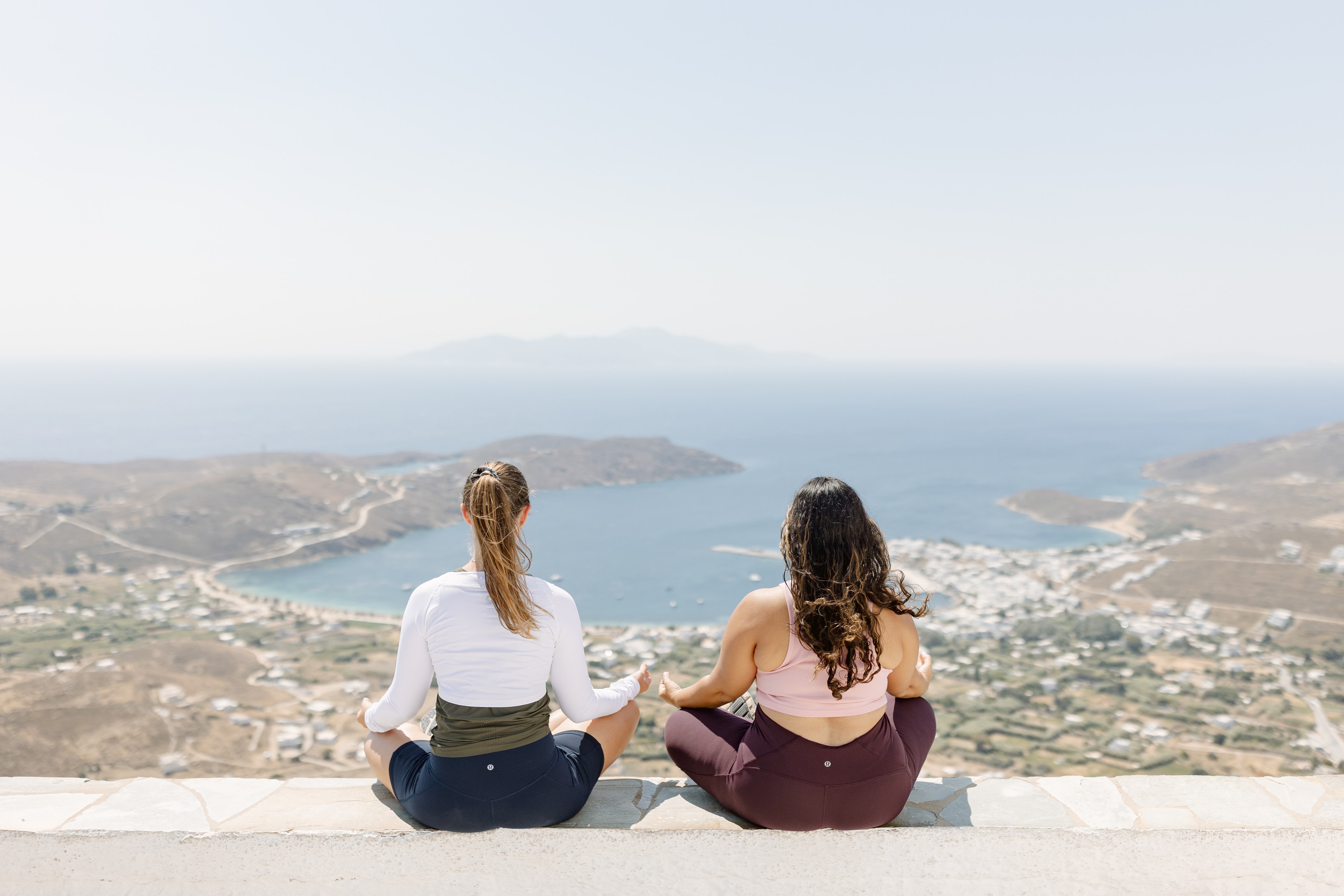 Advisor sitting on a look out point with her friend gazing out at a view with a city in the distance.