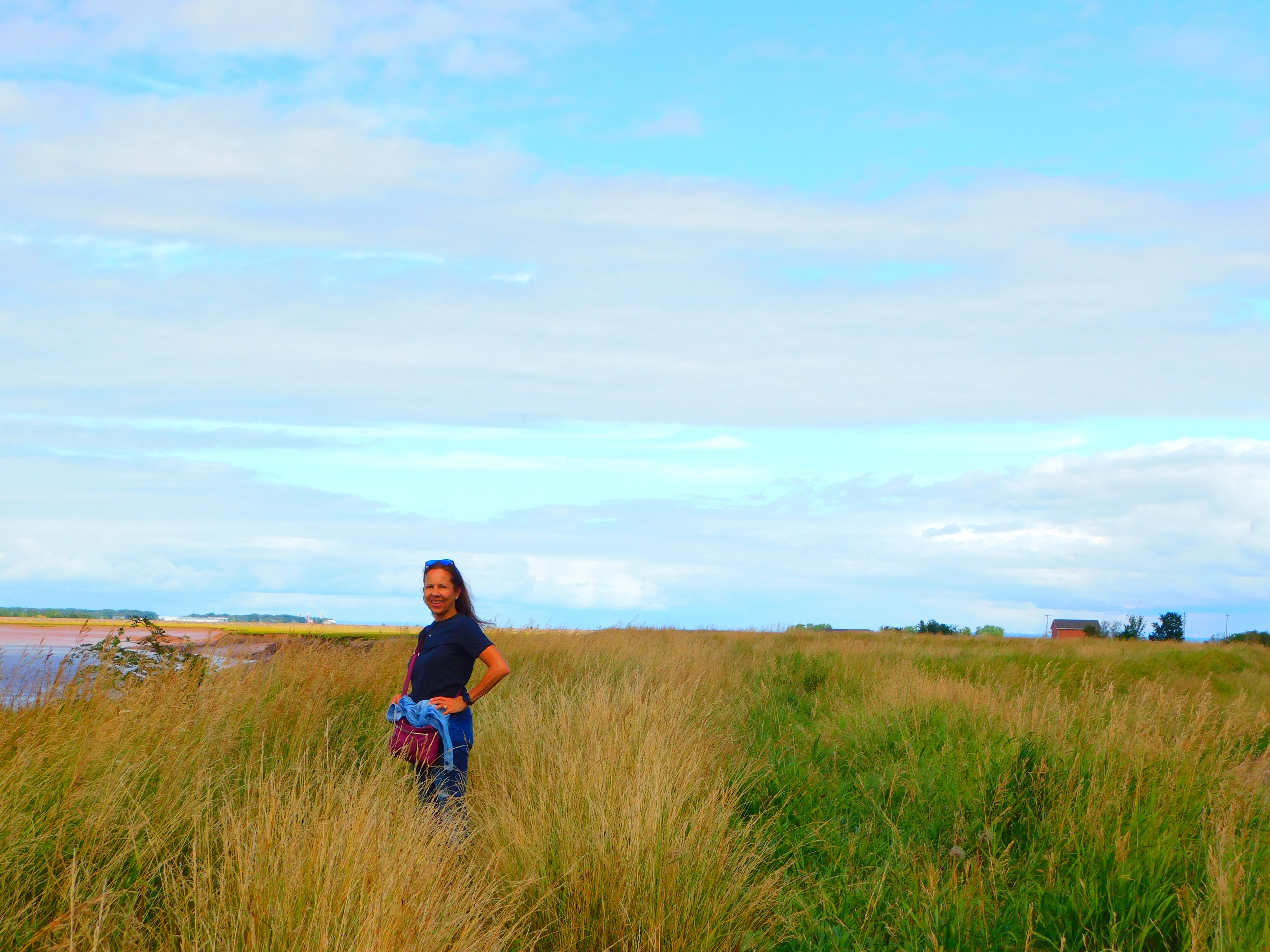 Isabel in a black shirt standing in an empty field of grass-like plants under sunny skies