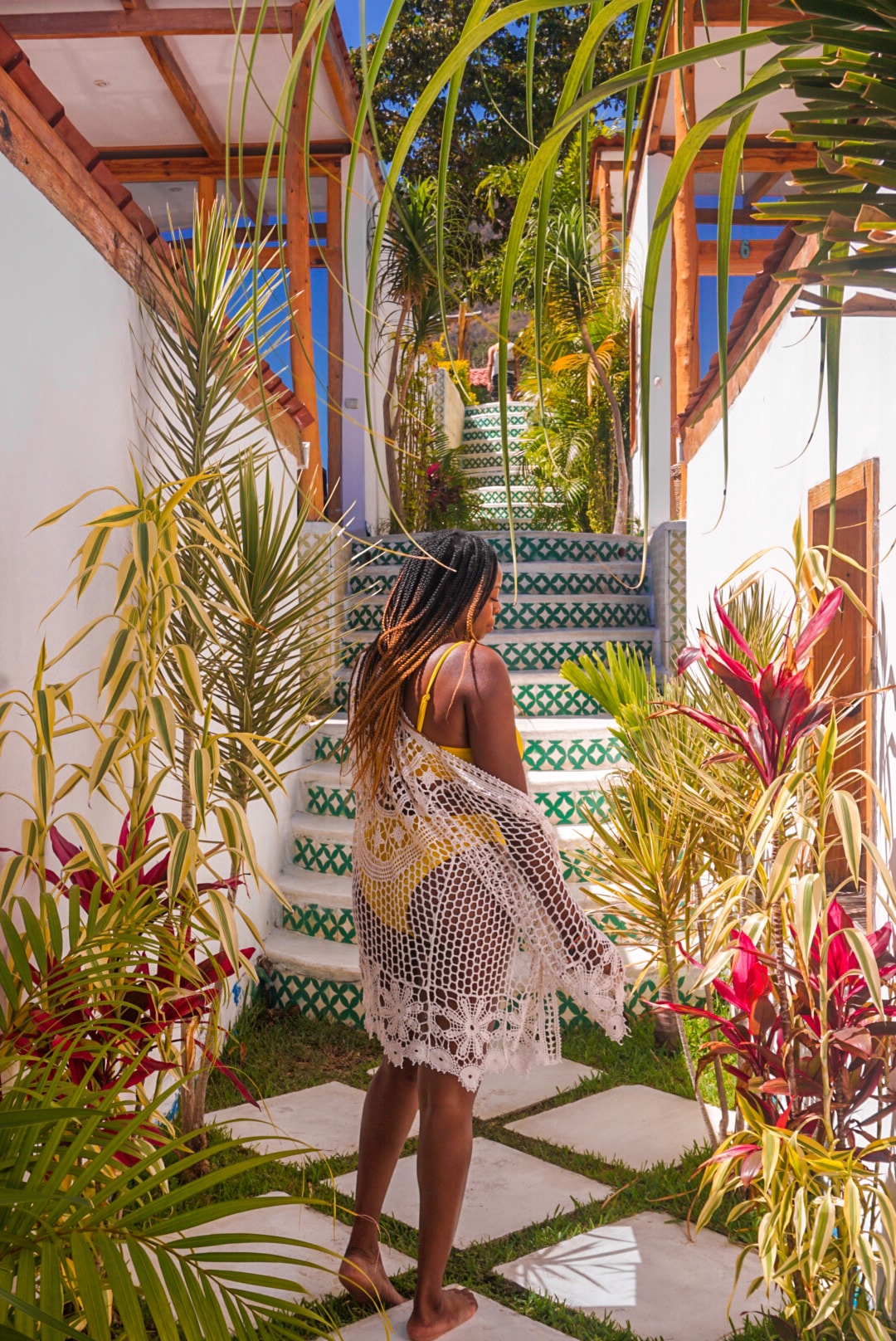 Denajia with bare feet walking along a white tile path surrounded by tropical plants