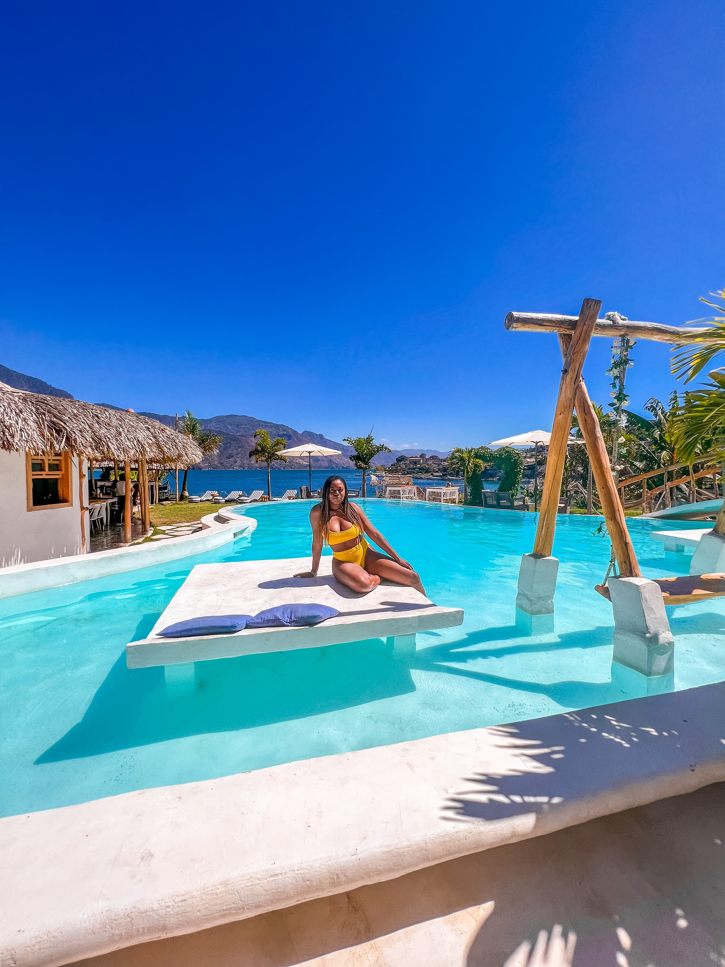 Danajia in a yellow bathing suit sitting on a white lounge in a pool on a sunny day