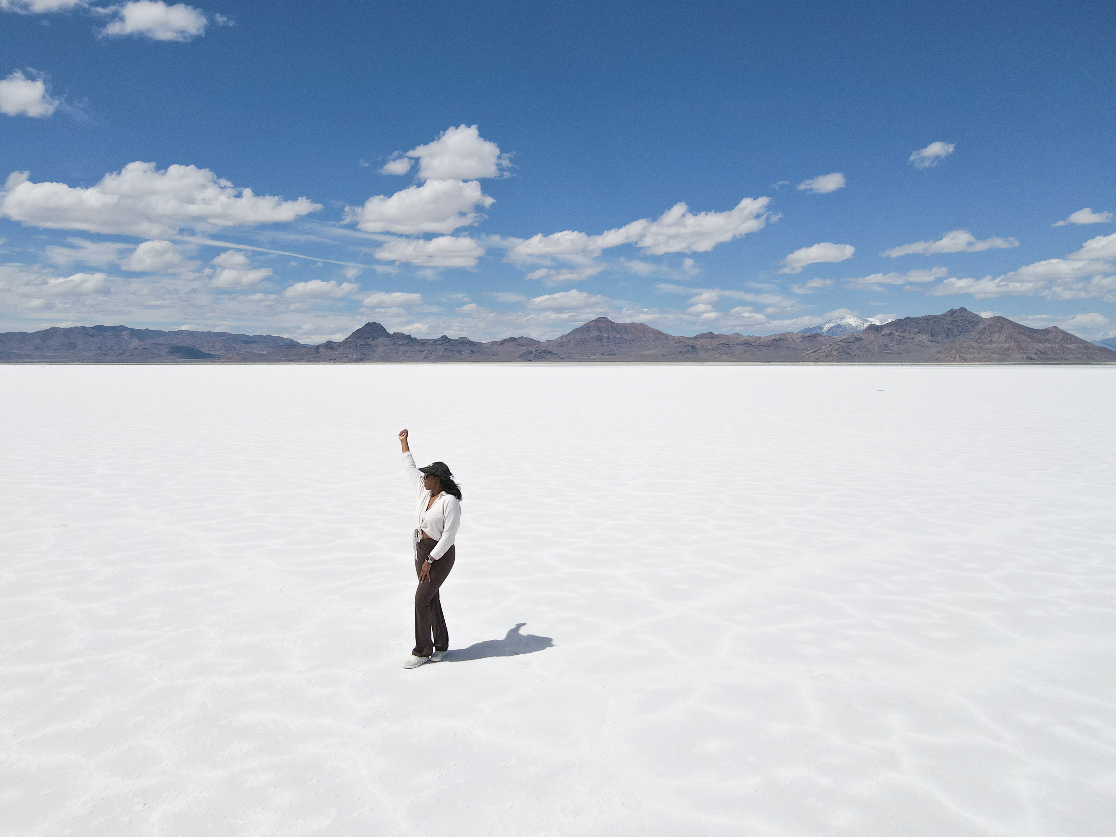 Denajia with her arm raised in the middle of an empty white salt flat landscape with mountains in the distance