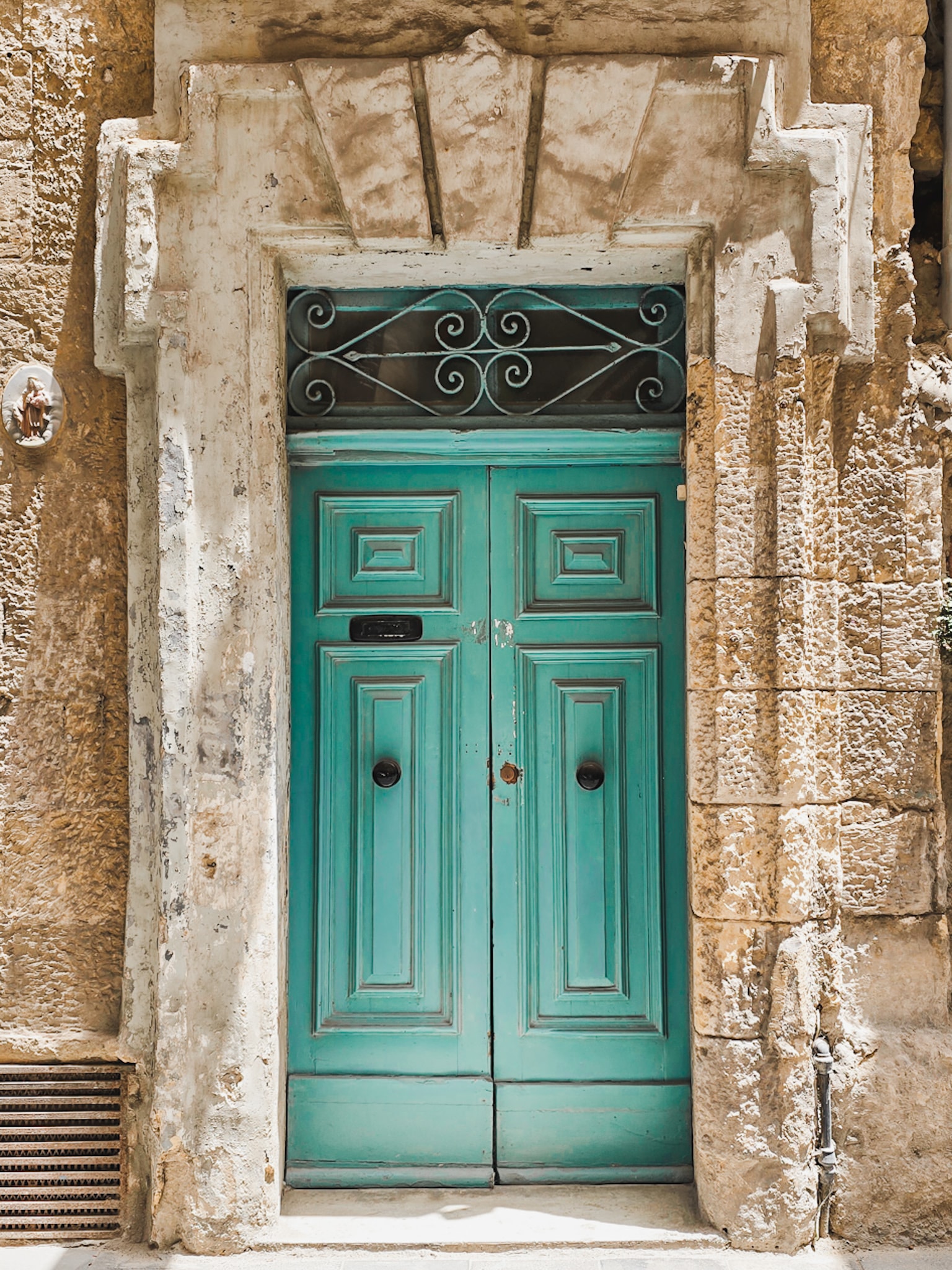 A turquoise set of french doors with rustic hardware and a sand colored building with geometric designs. 