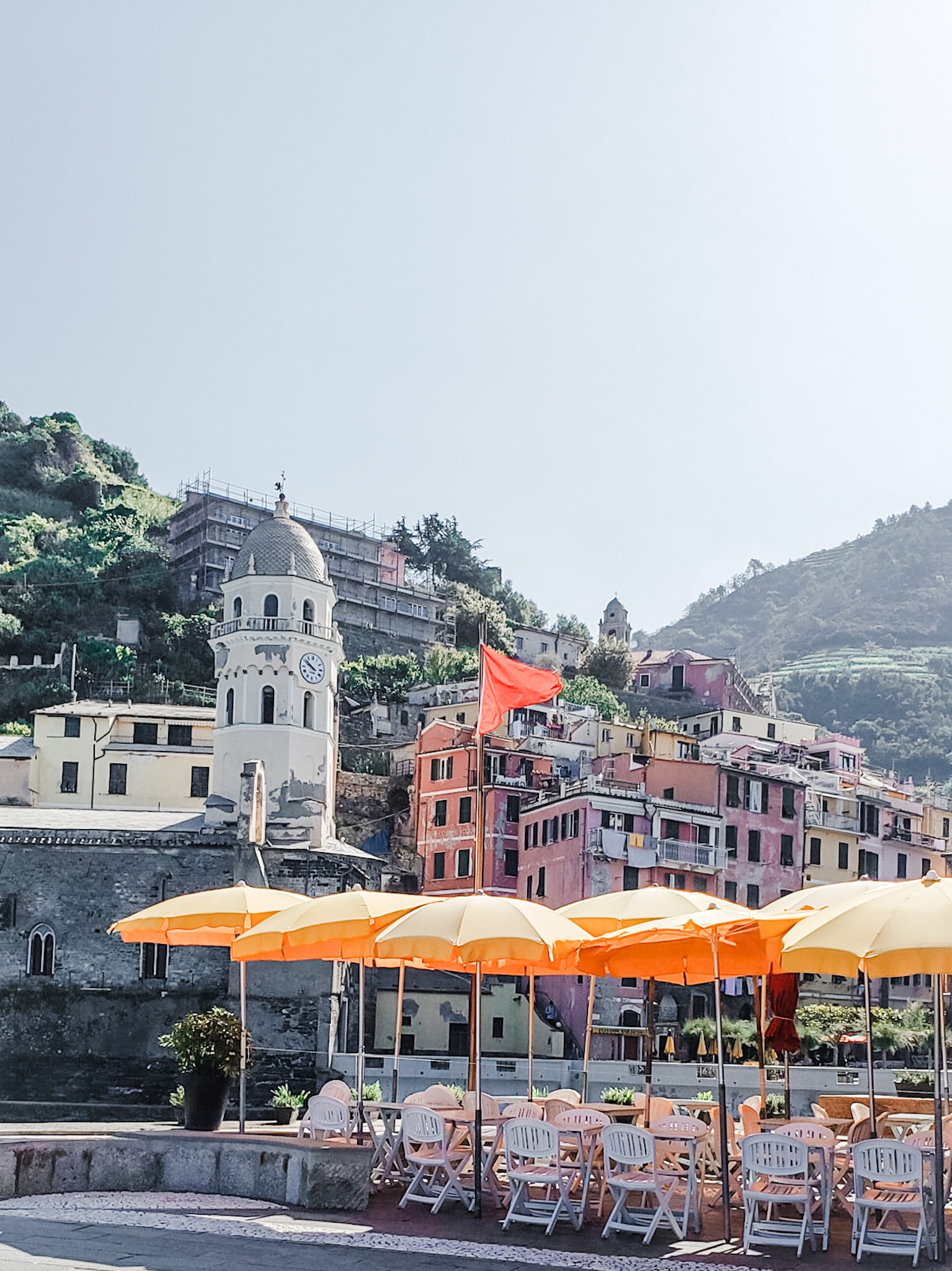 An outdoor patio with seating and sun umbrellas with a mountain scape and a town in the distance. 