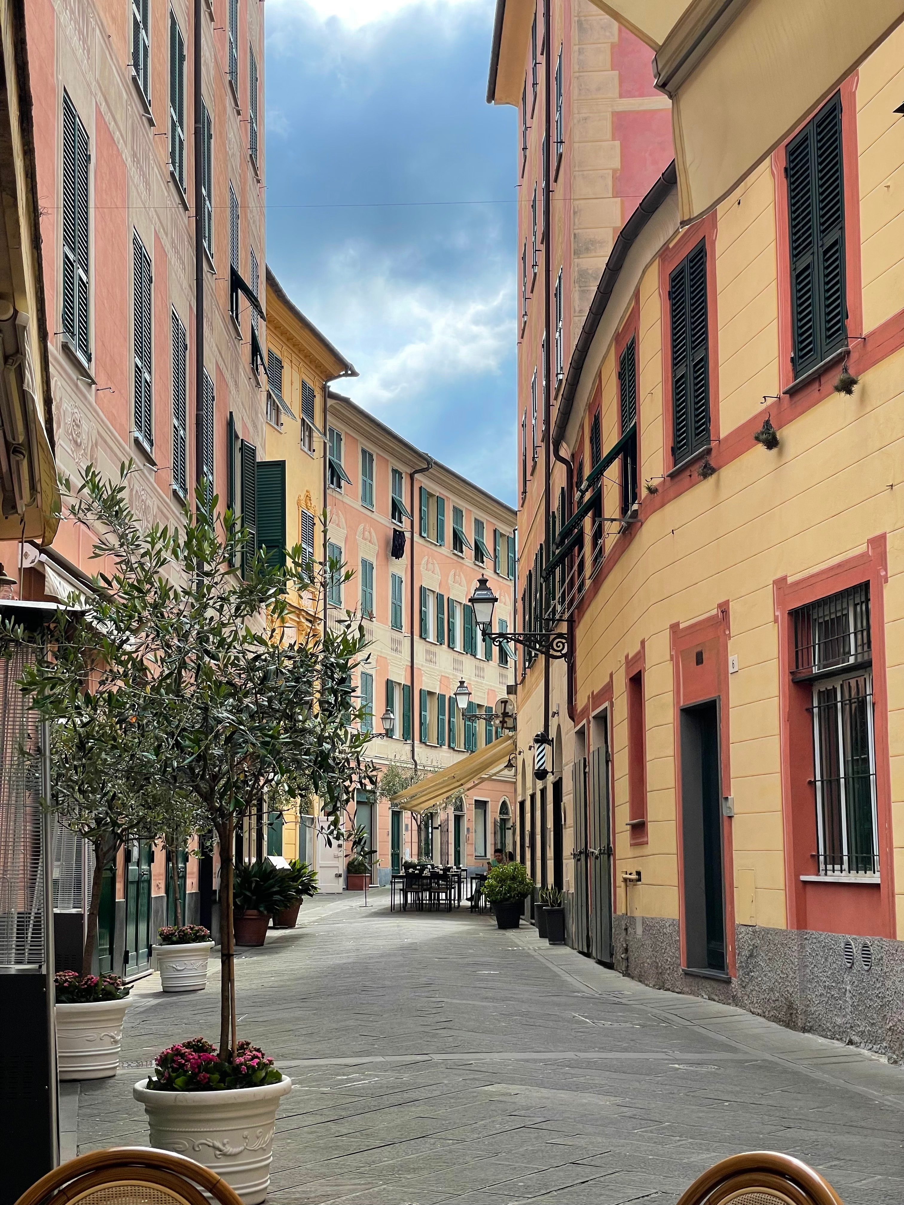 A narrow street with potted plants and colorful buildings on a sunny day.