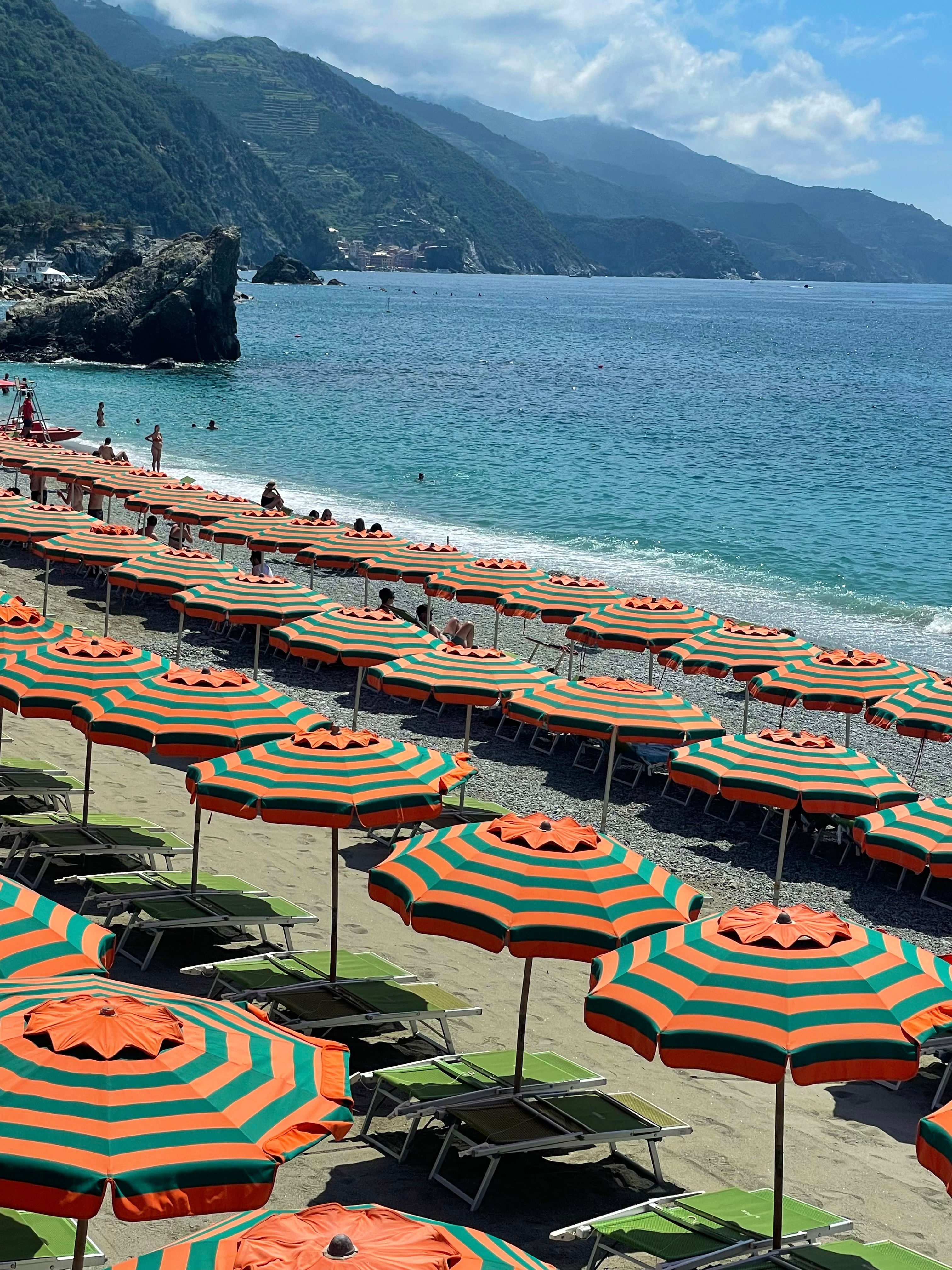 A view of a shoreline at the beach with a beach club that has sun umbrellas and loungers on a sunny day.