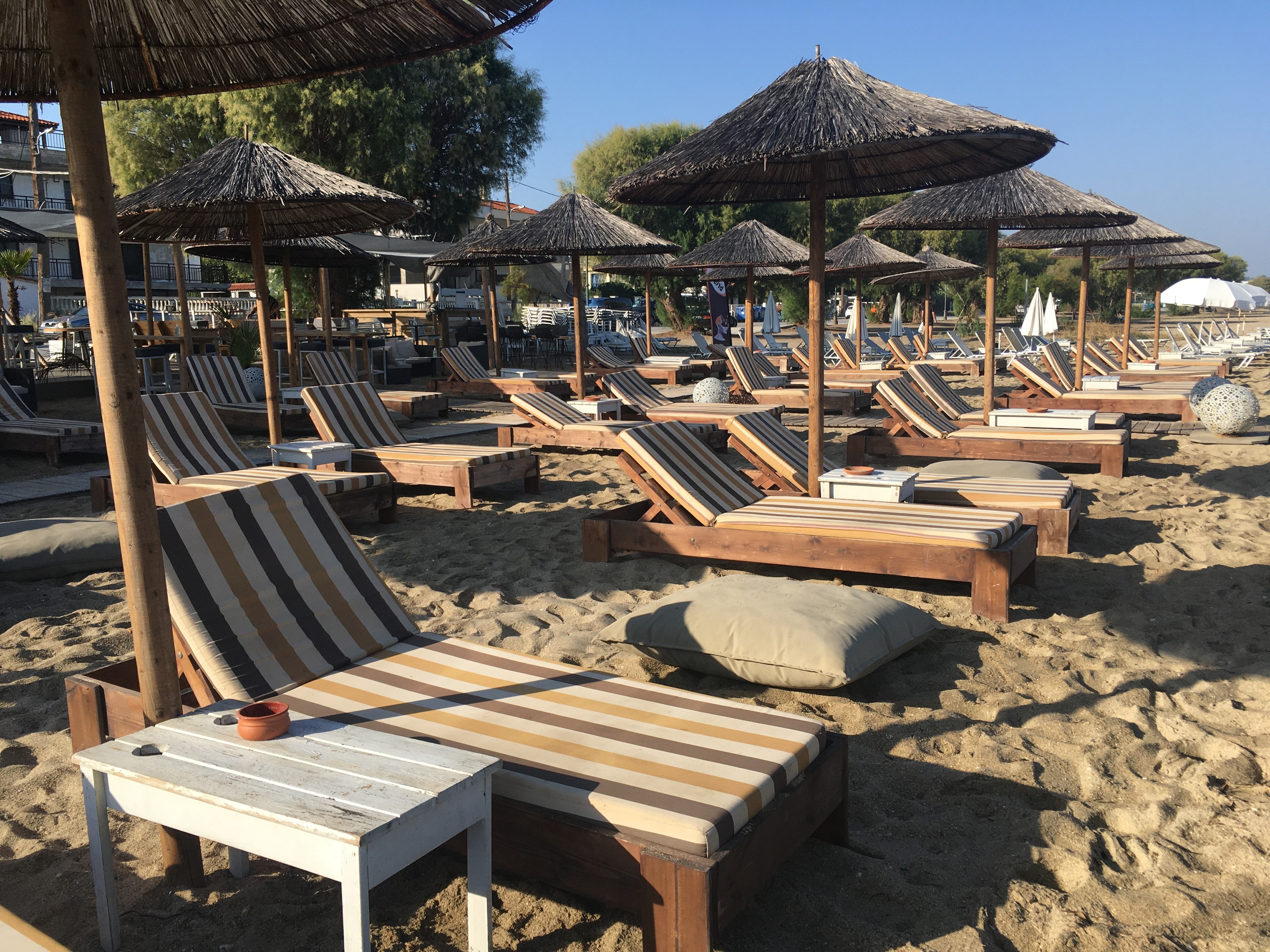 A view of a beach with striped lawn chairs, umbrellas and tables. 