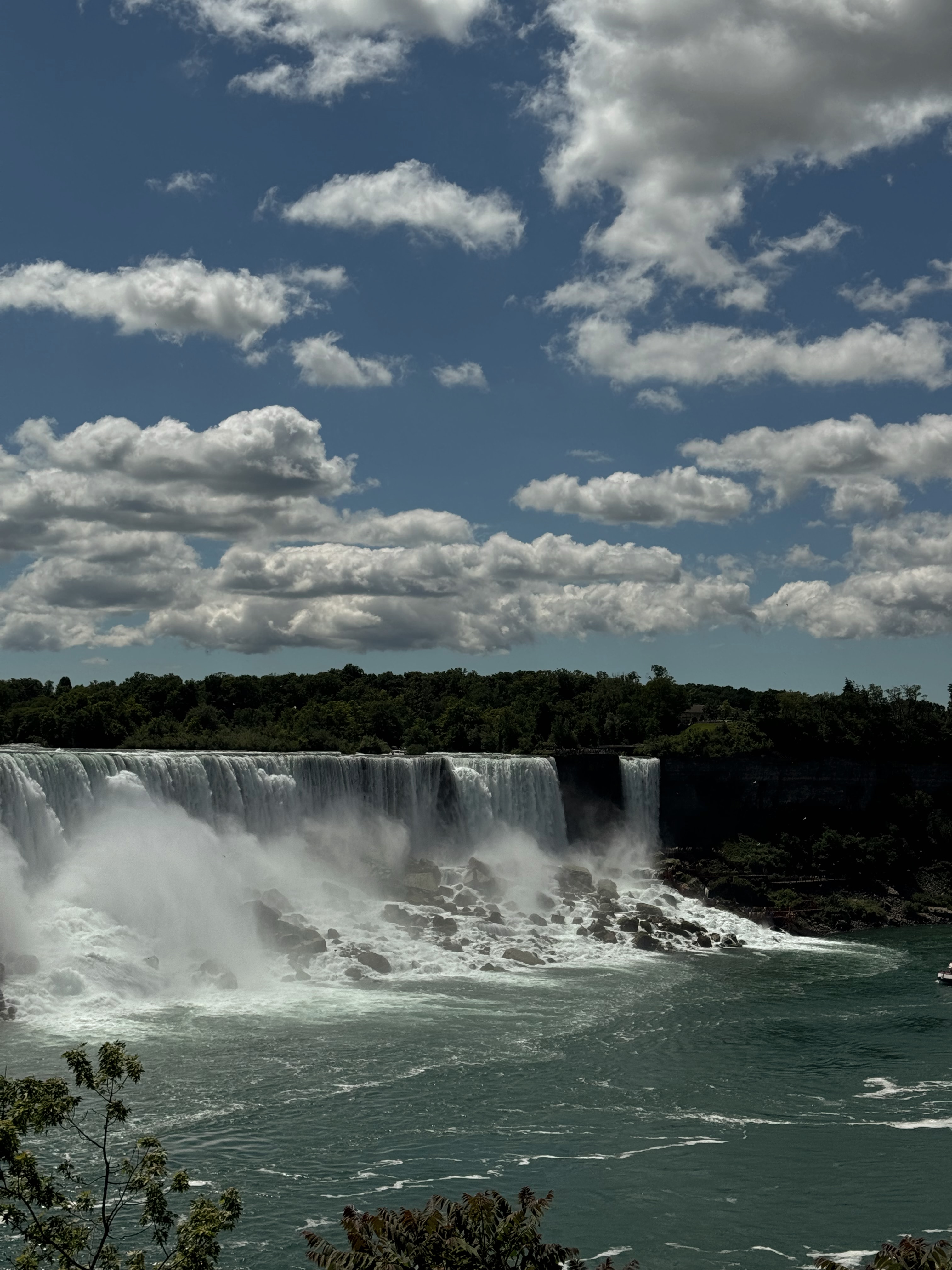 View of a very large waterfall pouring into a body of water surrounded by hills on a sunny day