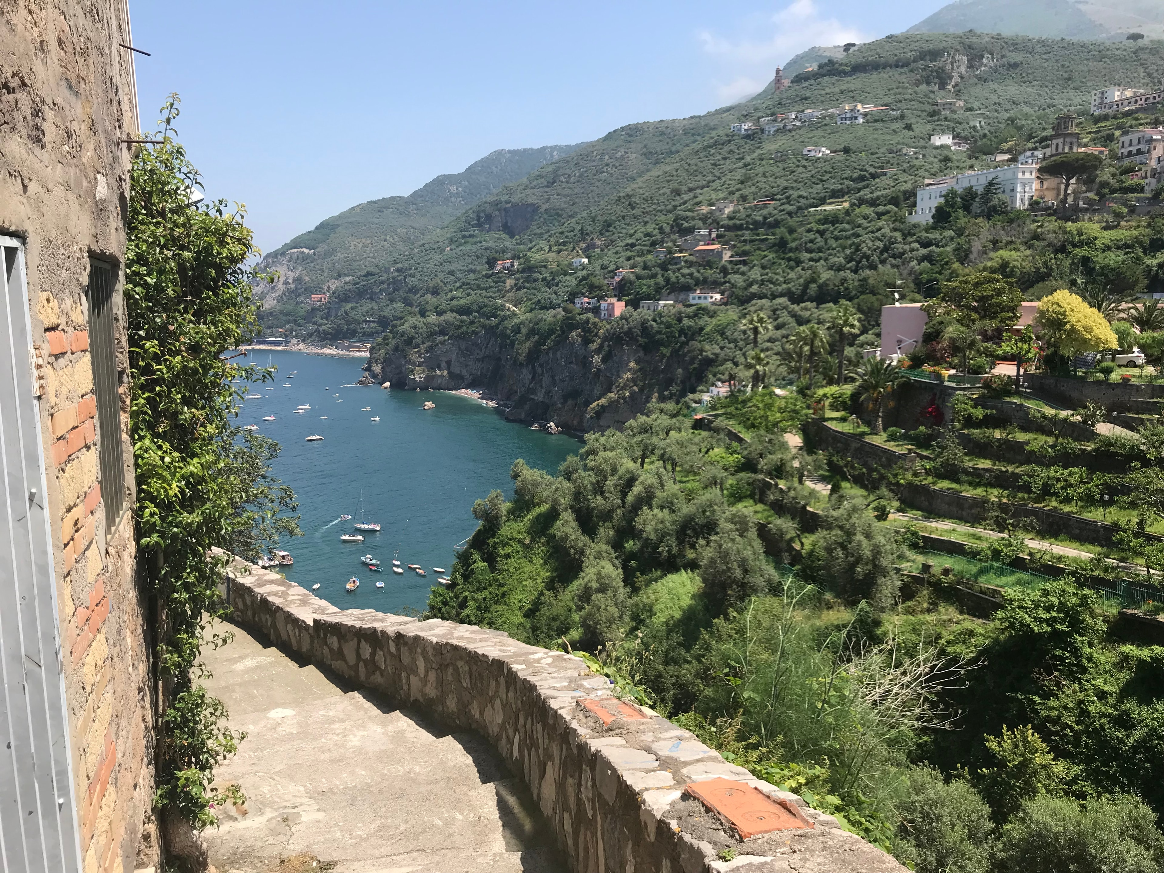 Beautiful view of a sunny, green hilly coastline leading to the sea where small boats float offshore