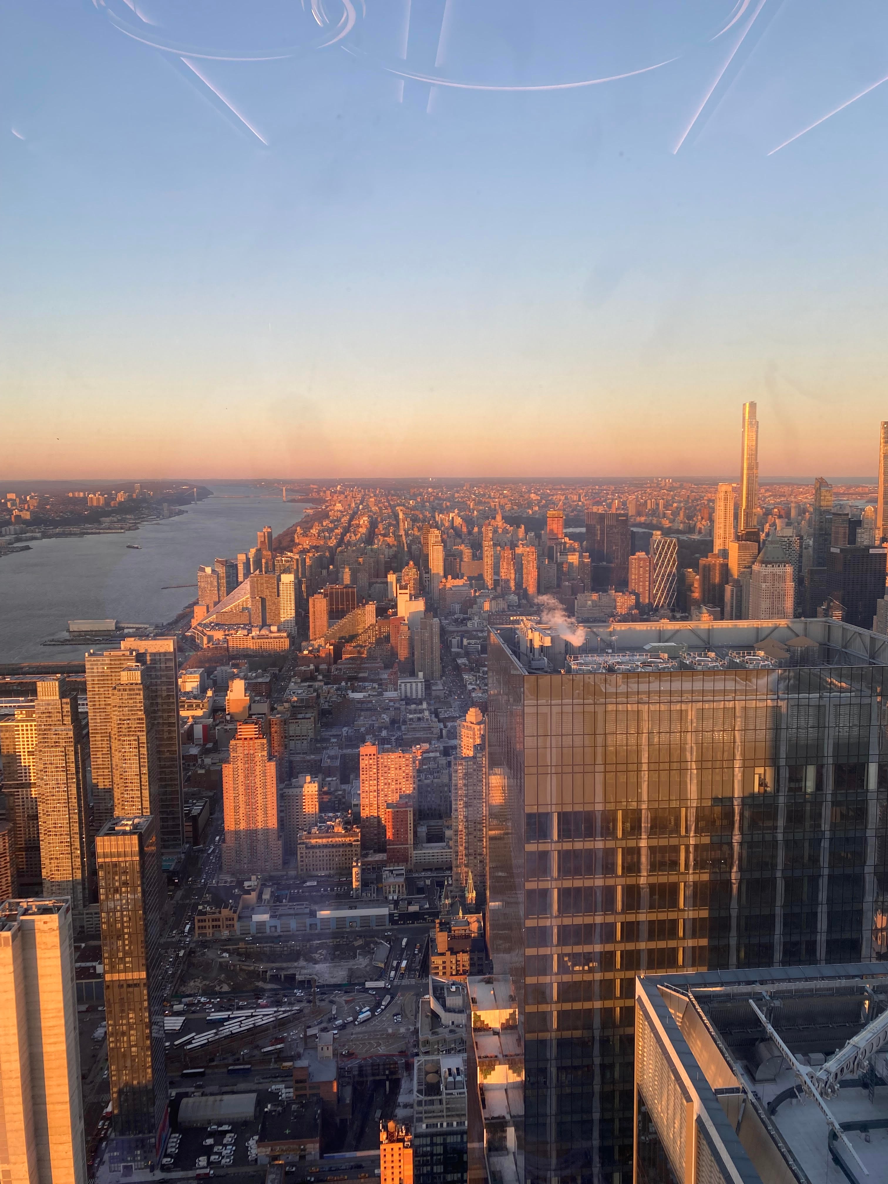 A view of New York city from a look out point at dusk with a large river in the distance. 