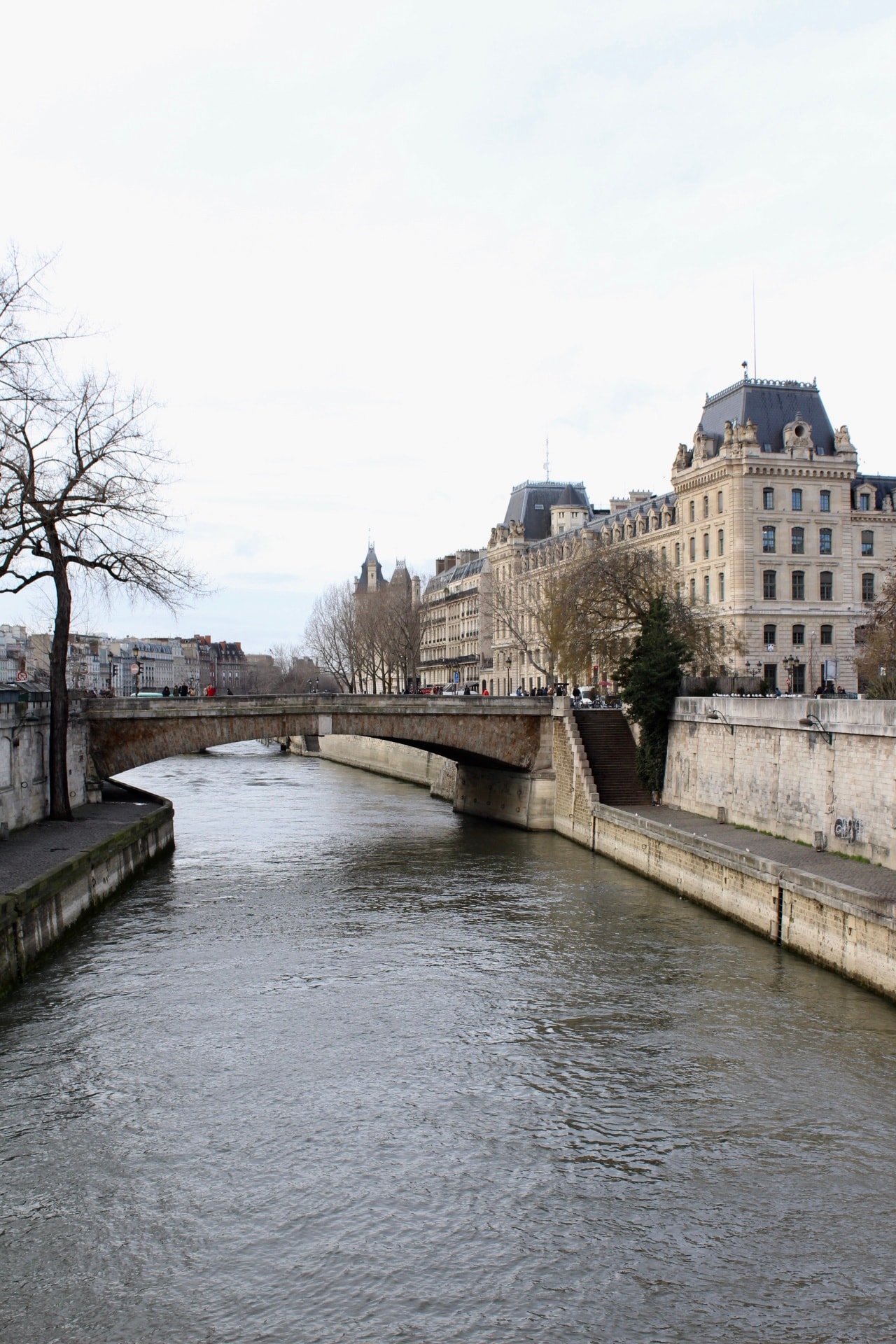 View of a river with a bridge connecting stone pathway with buildings and trees on either side