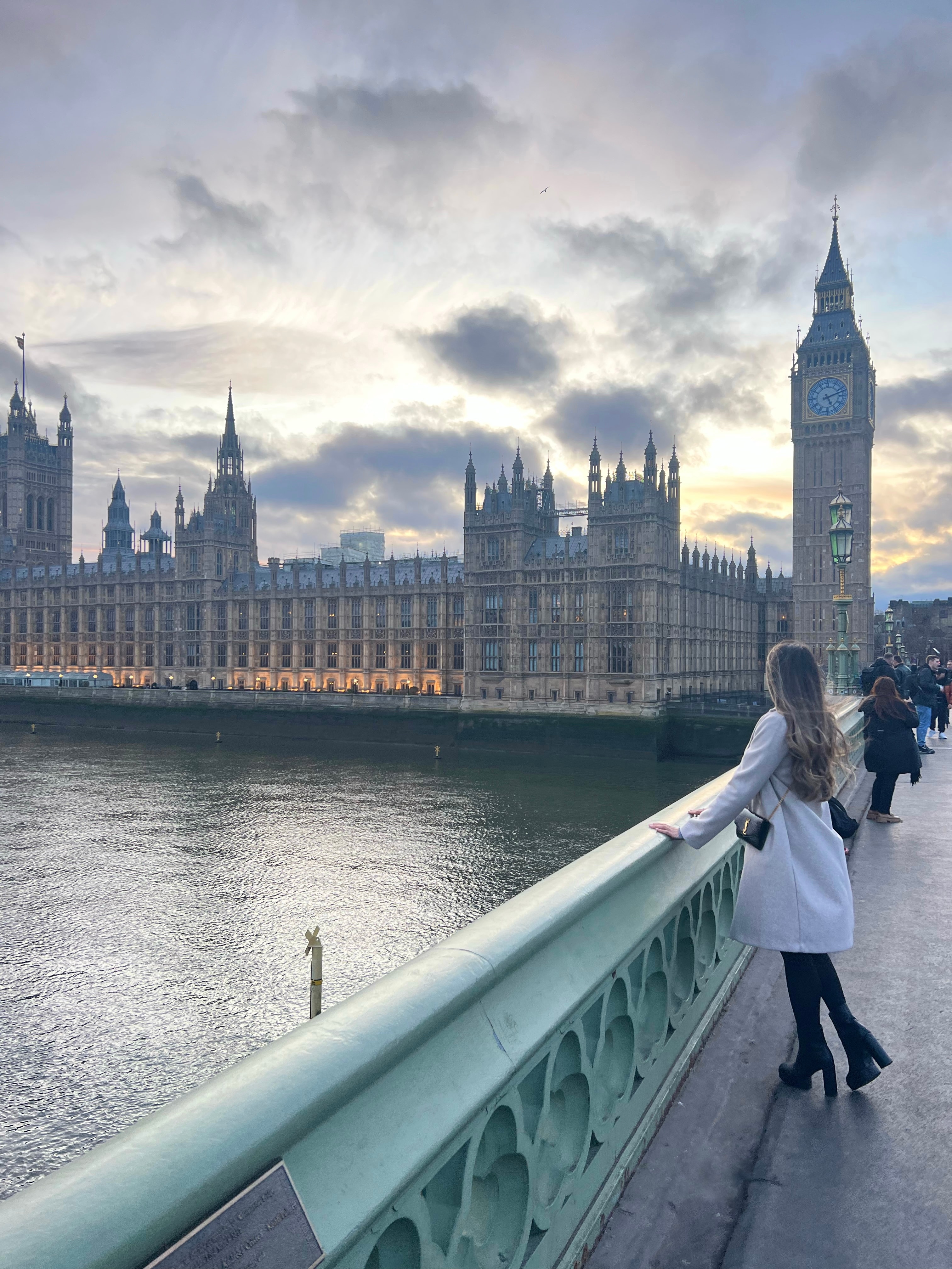 Advisor on a bridge overlooking a view of Big Ben near the water on a cloudy day. 