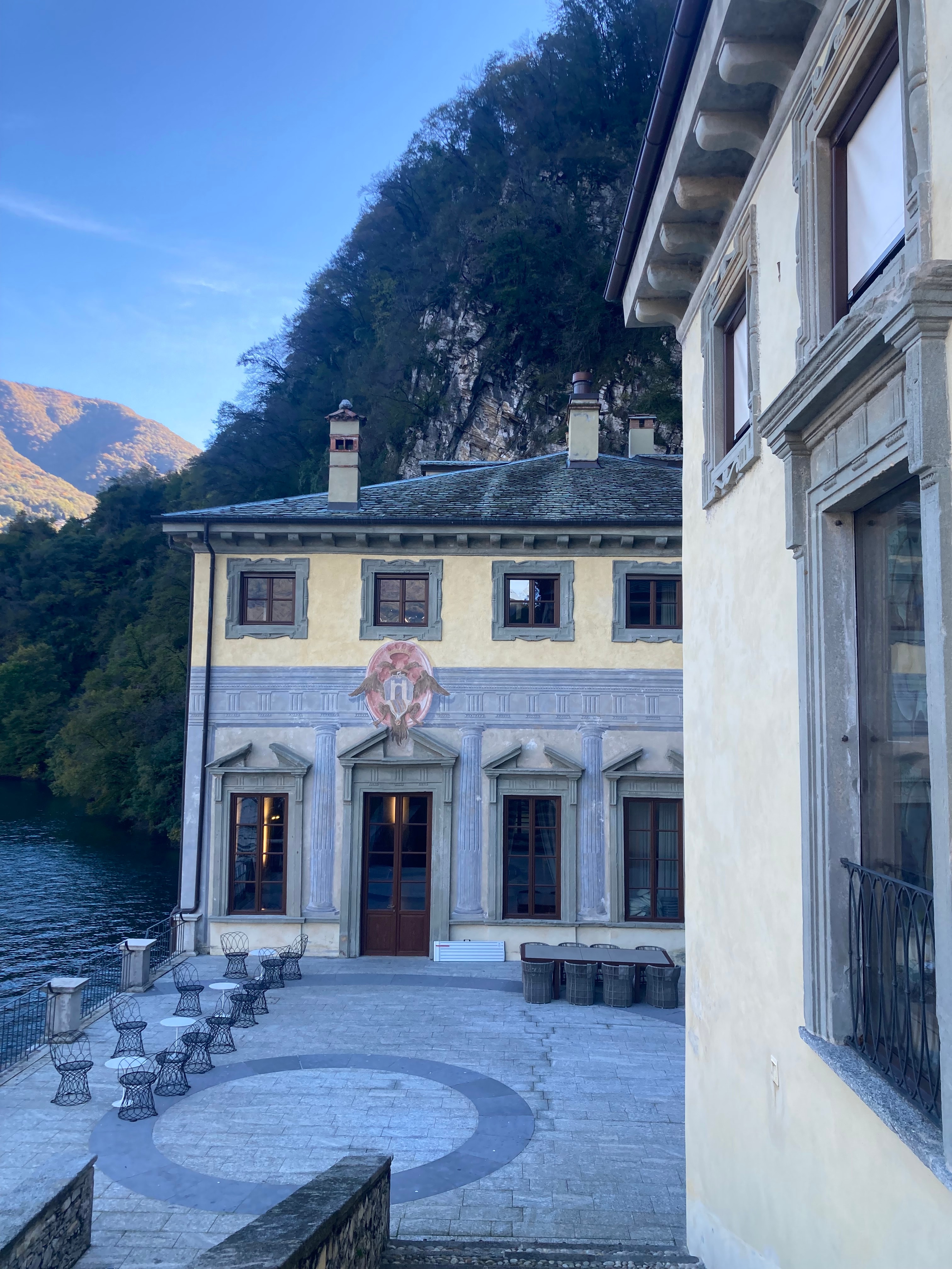 A outside view of a luxurious hotel at dusk with classic architecture surrounded by foliage. 