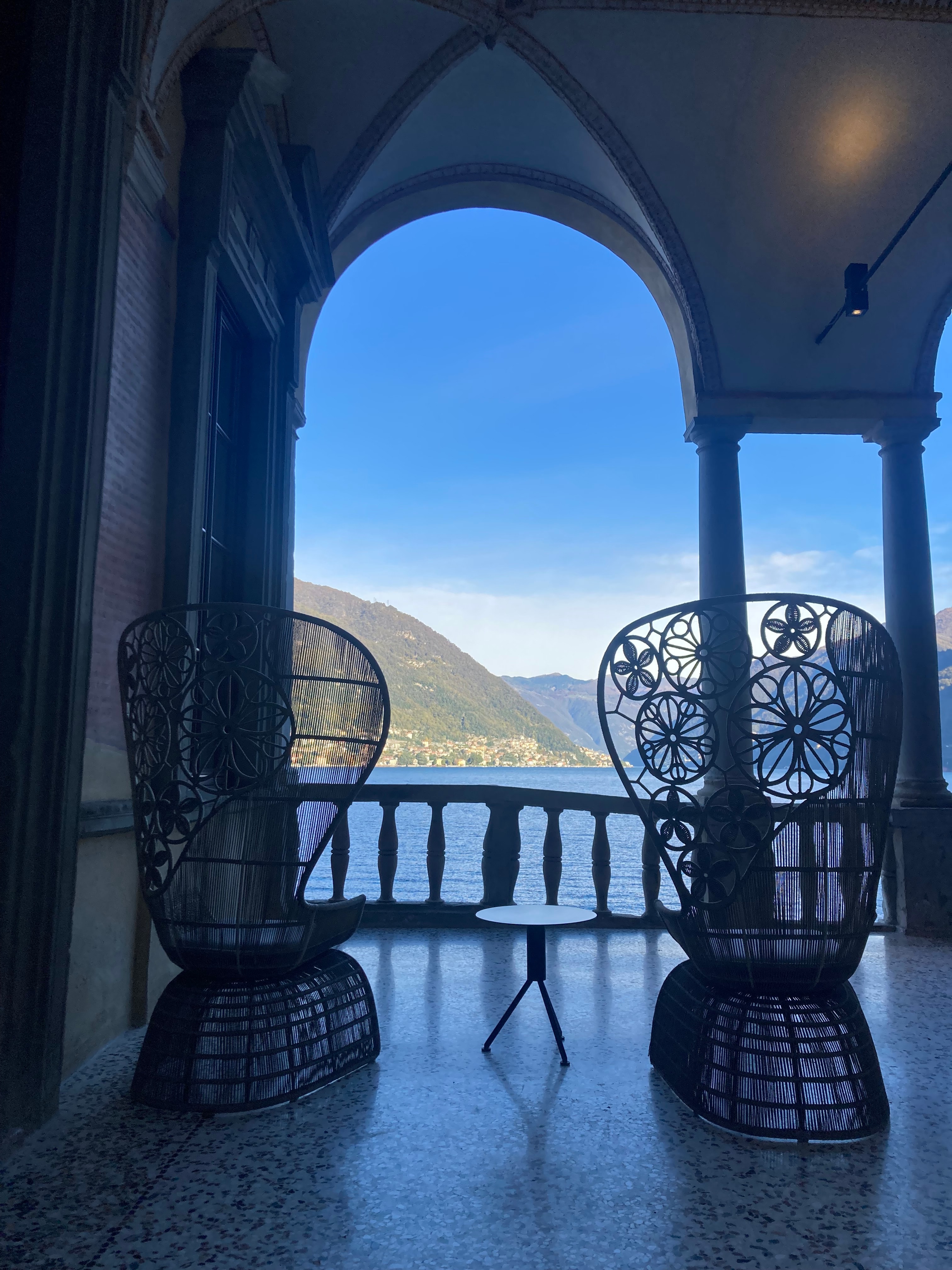 The inside of a seating area with large chairs and a balcony with the ocean and a mountain range in the distance.